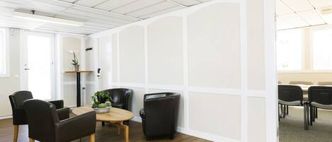 A modern meeting room with a wooden table, black chairs, and a white partition wall.