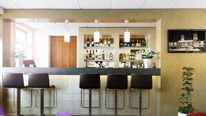 Zona de bar con mostrador, varios taburetes y un televisor en la pared que muestra una escena de hotel.