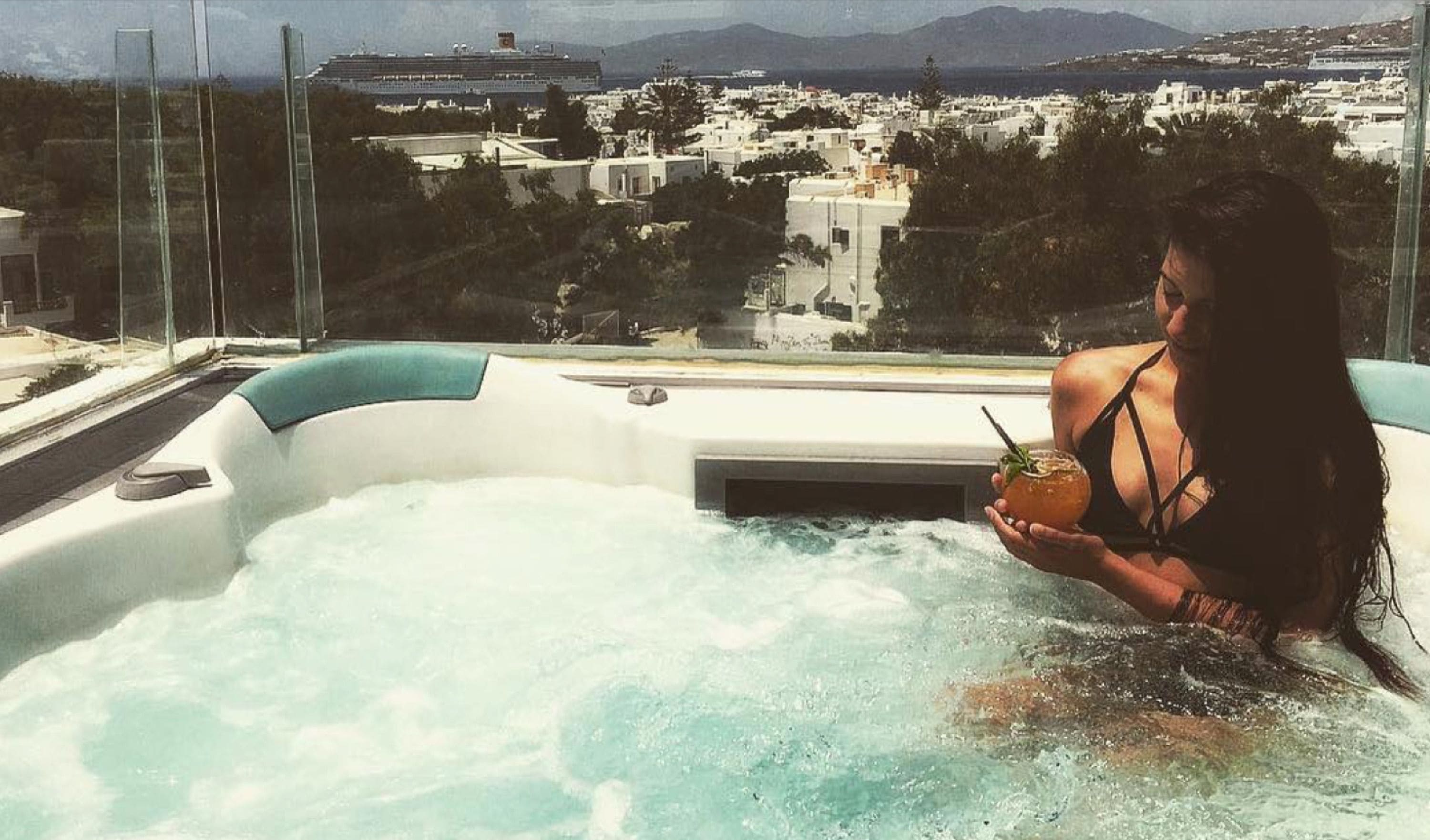 A person in a hot tub with a view of a cityscape and mountains in the background.