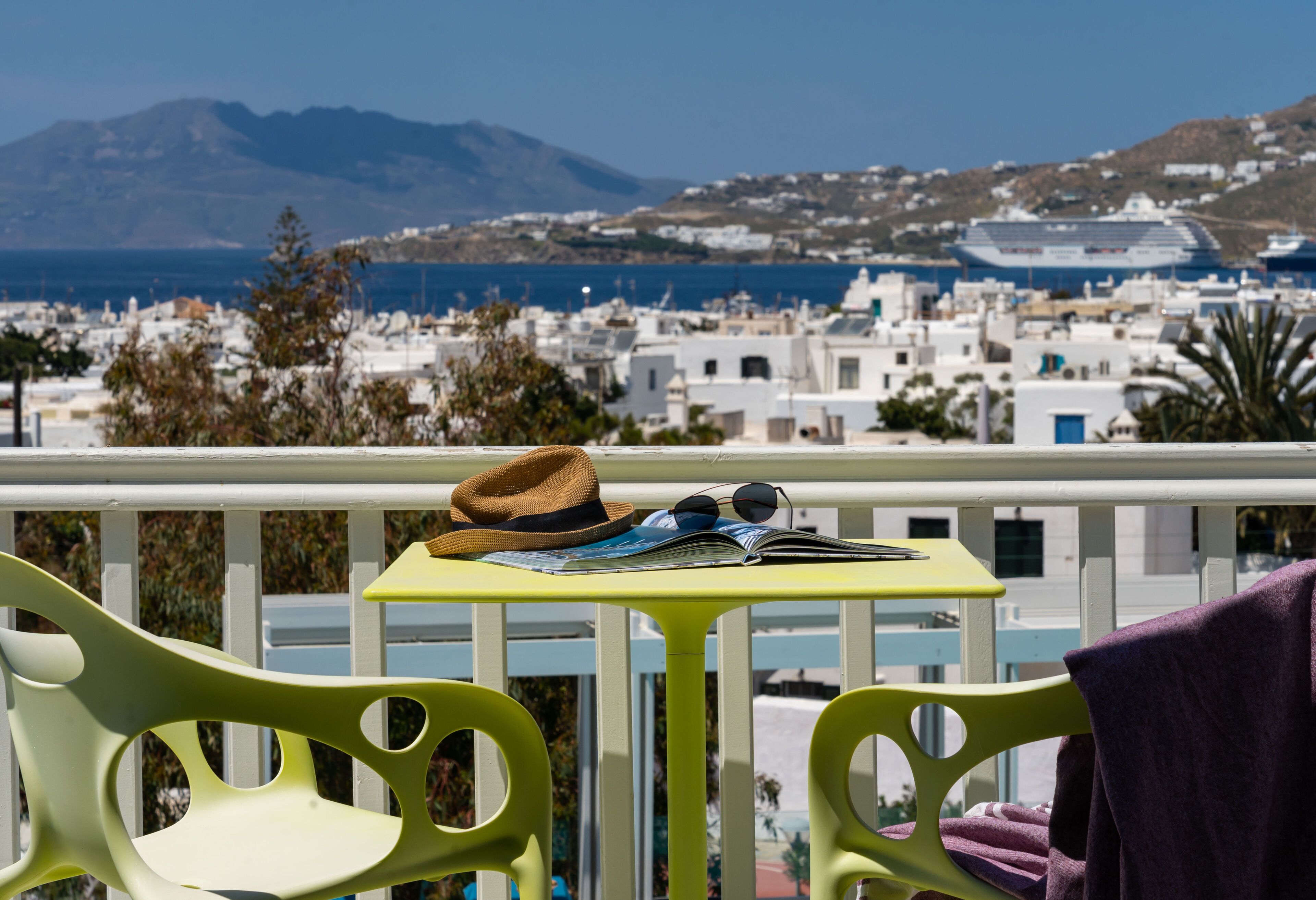 Un balcon avec une table, des chaises et une vue sur une ville côtière, avec des bâtiments et une montagne en arrière-plan.