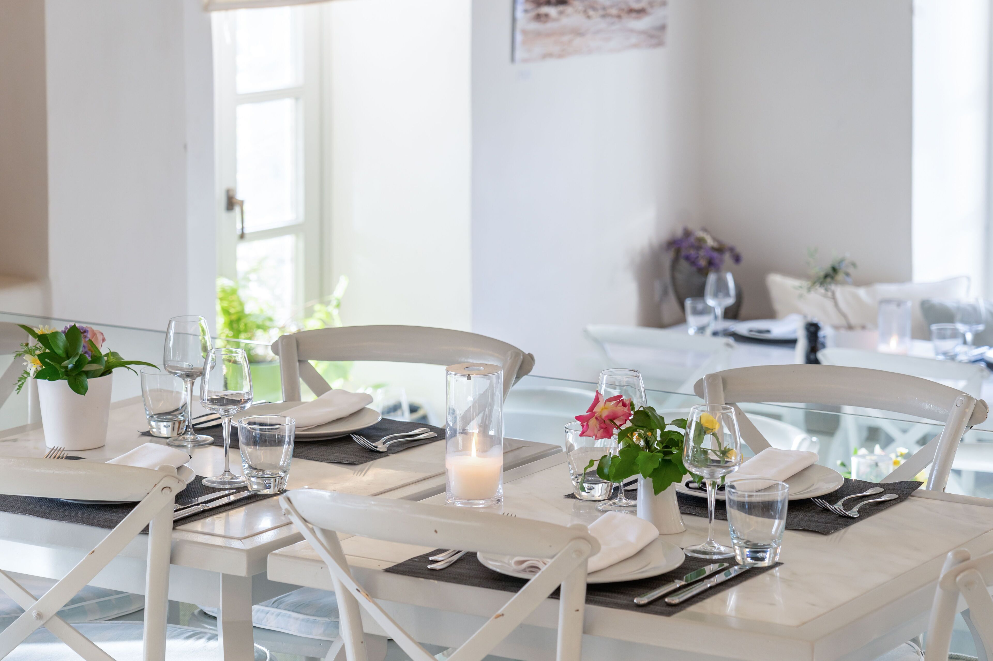 A dining table set with white chairs, plates, cutlery, glasses, and a candle.