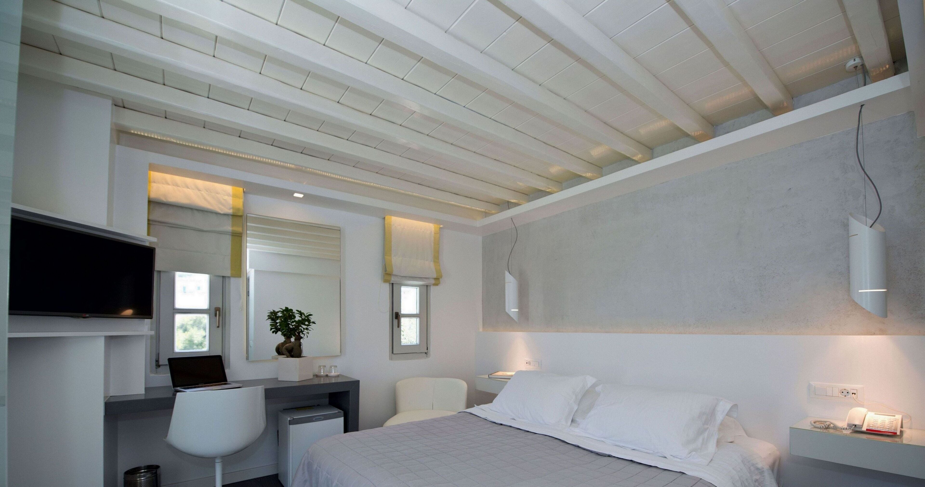 A modern bedroom with a bed, a desk, a chair, a television, and a window.