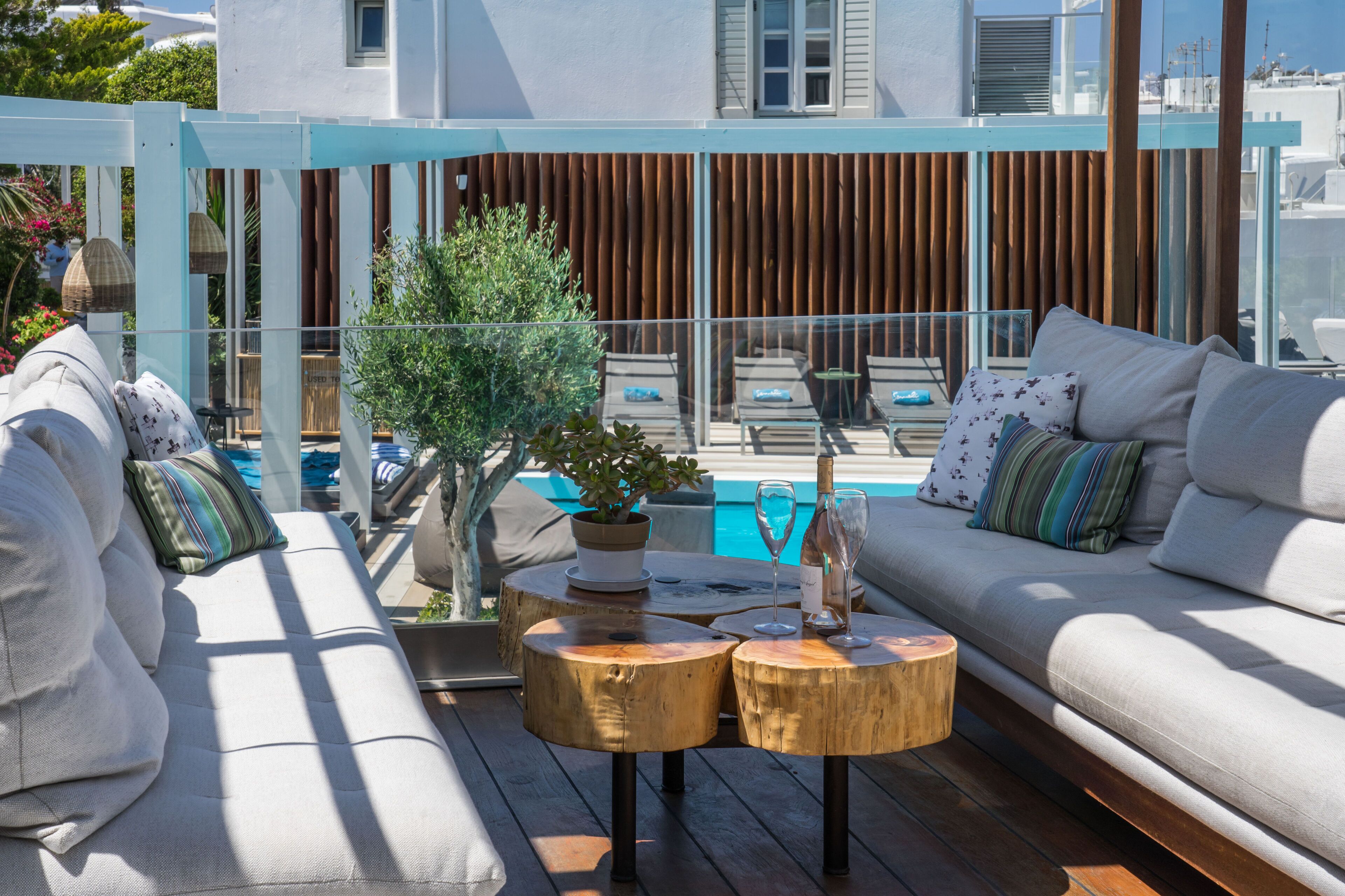 A sunlit outdoor seating area with a pool in the background, wooden tables, and a modern building facade.