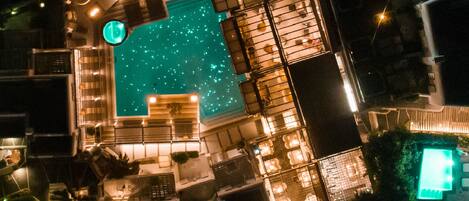 Vista aérea de un hotel con piscina, varios balcones e iluminación exterior.