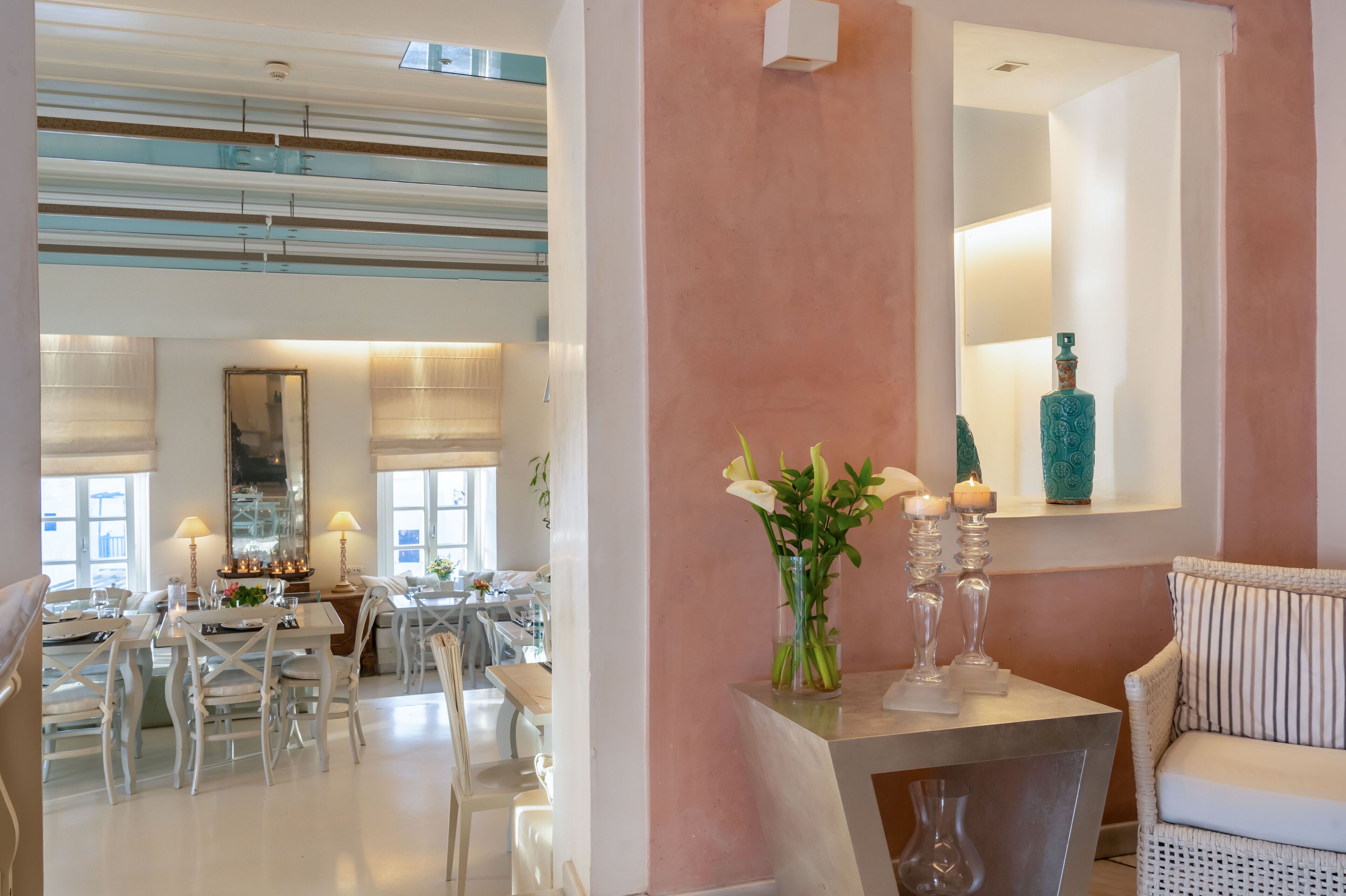 A modern dining area with white furniture, a central mirror, and a vase with flowers.