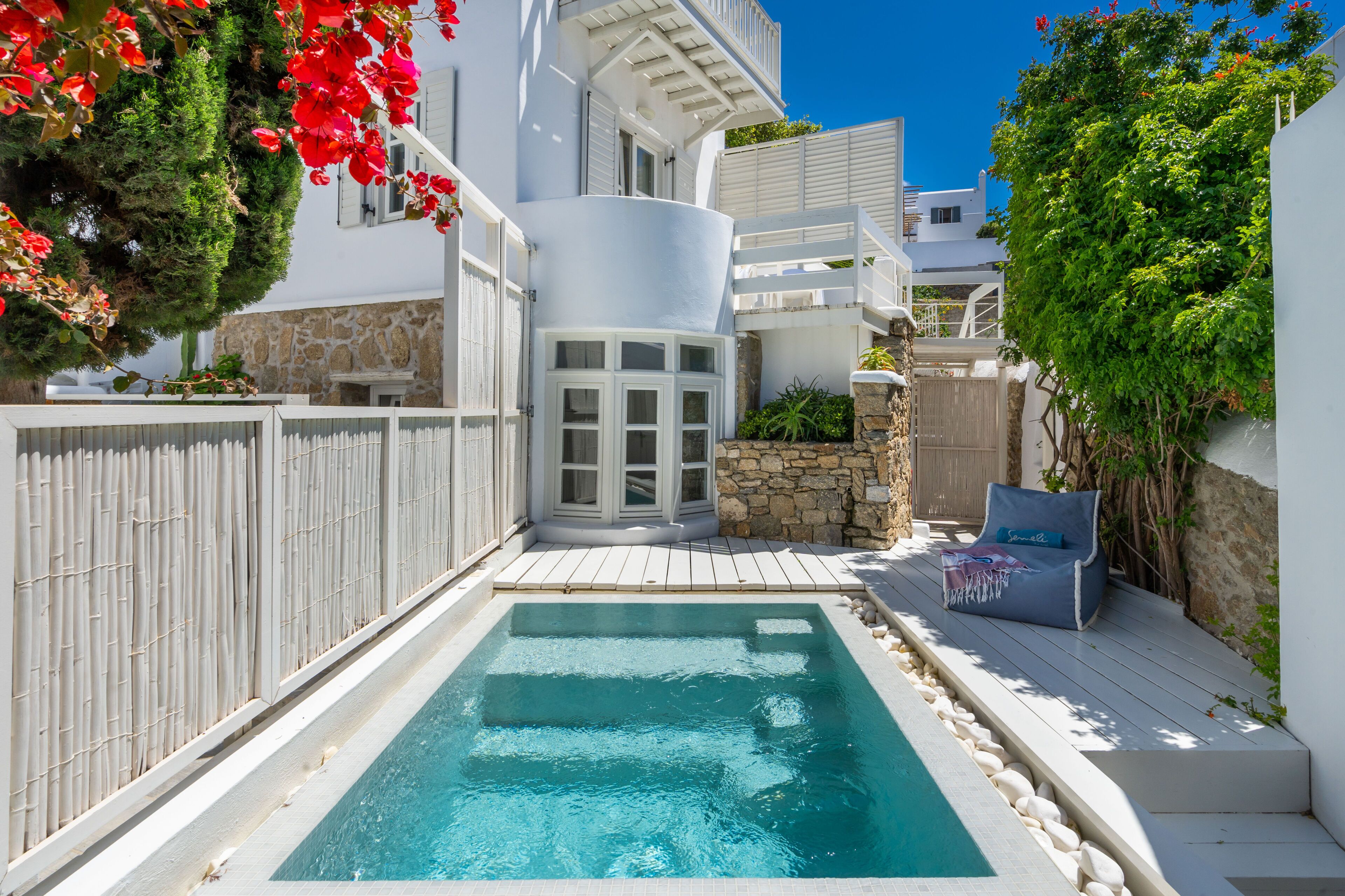 A swimming pool surrounded by a white fence, a stone wall, and a wooden deck with a chair.
