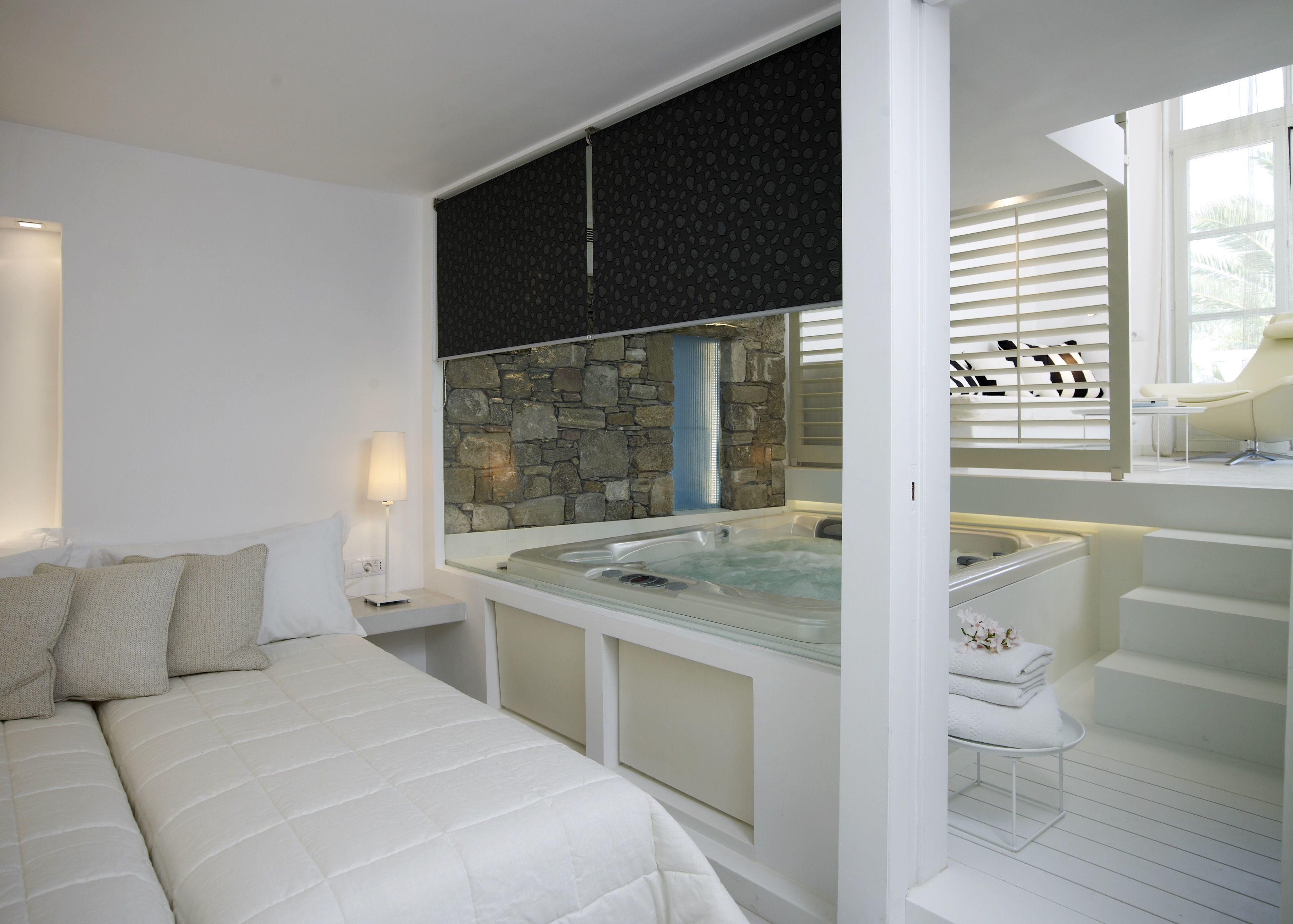 Un dormitorio moderno con una cama grande, un jacuzzi con paredes de cristal y una pared de acento de piedra.
