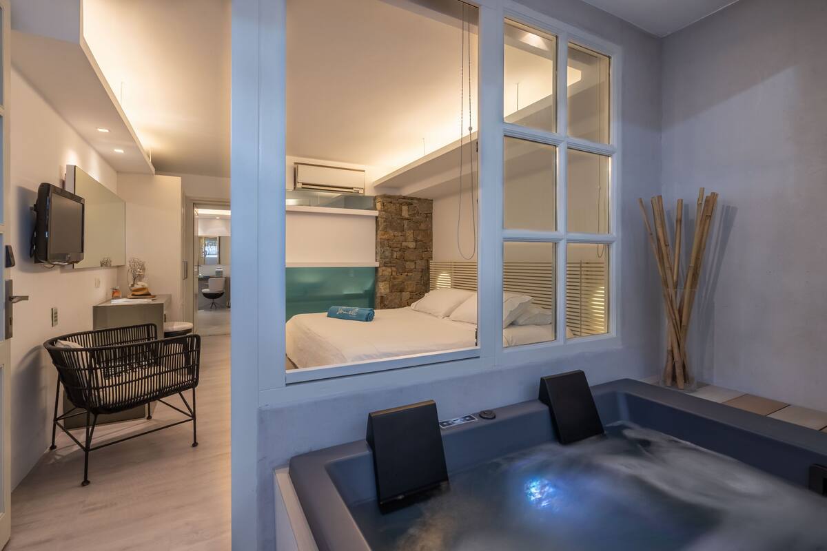 Una habitación moderna con un gran ventanal, una bañera de hidromasaje, una cama y una zona de estar.