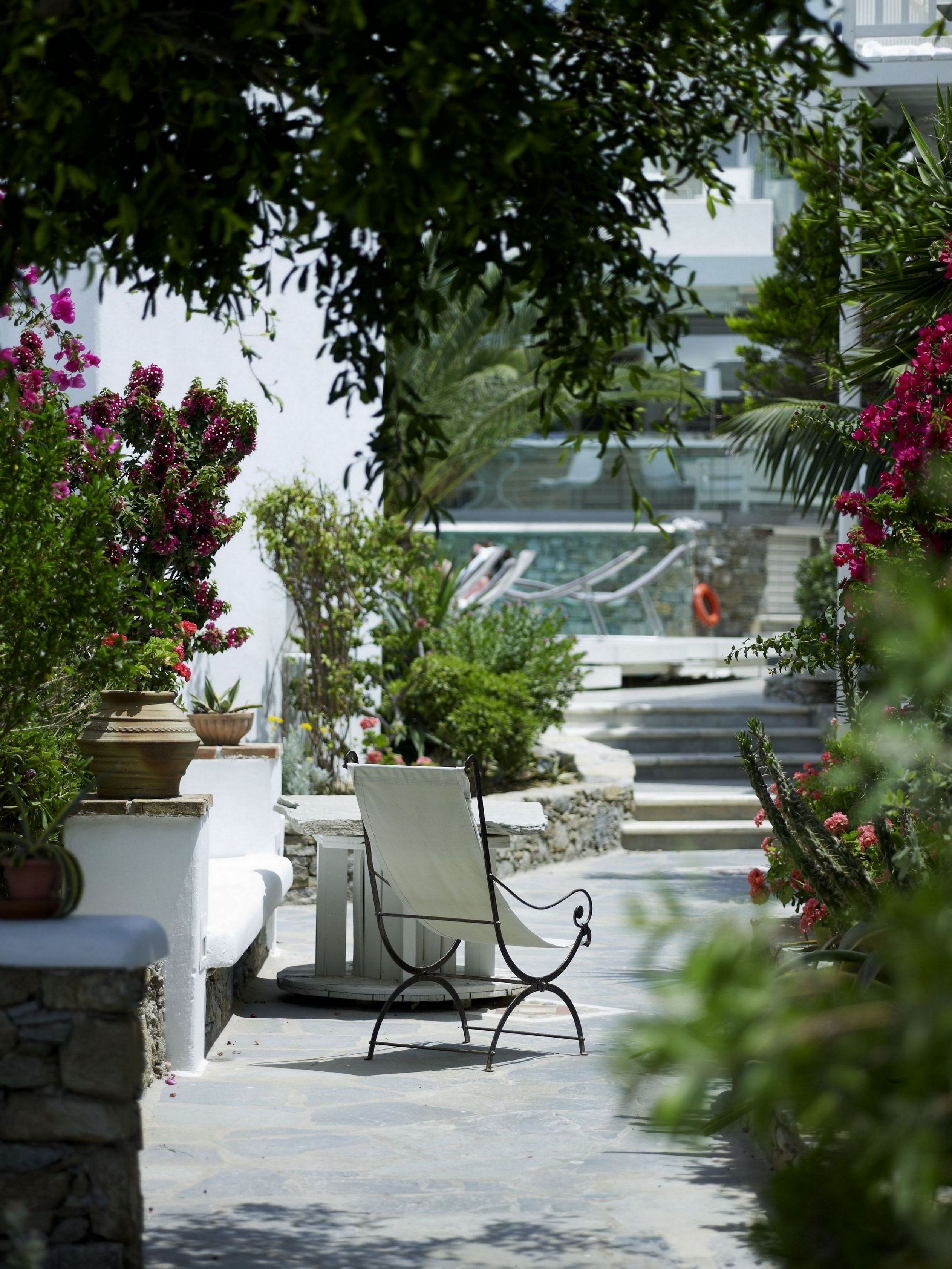A serene outdoor seating area with a chair and a table, surrounded by lush greenery and flowering plants.