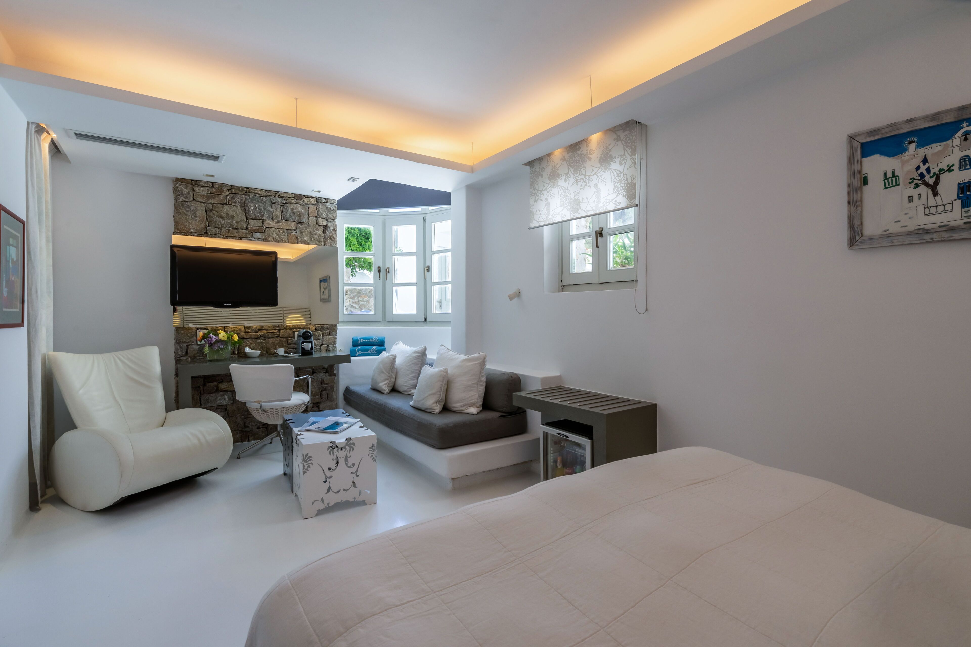 A modern bedroom with a large bed, a sofa, a chair, and a small table. There is a stone wall and a window with a view.