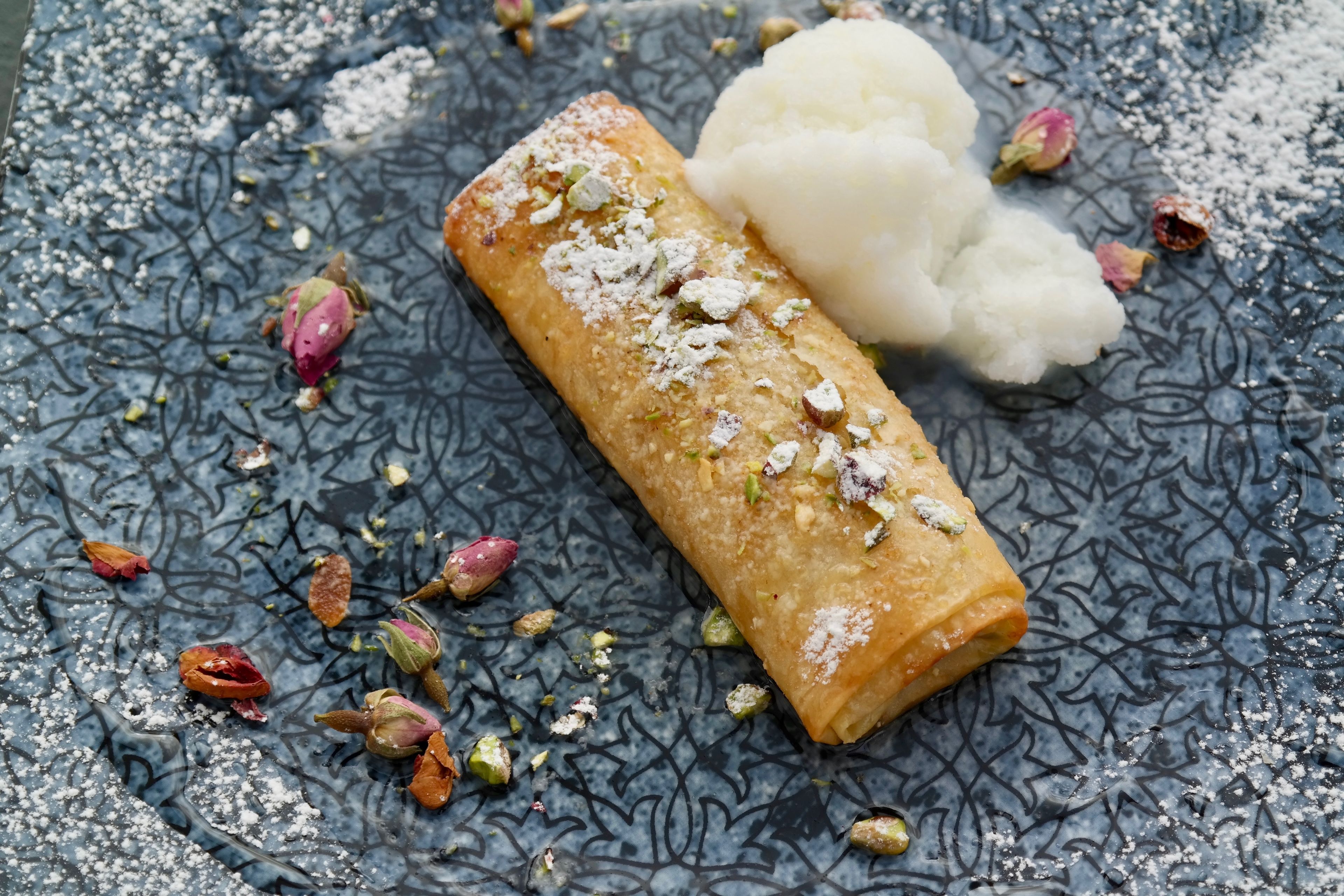 A dessert with a rolled pastry and a scoop of ice cream on a textured blue plate.