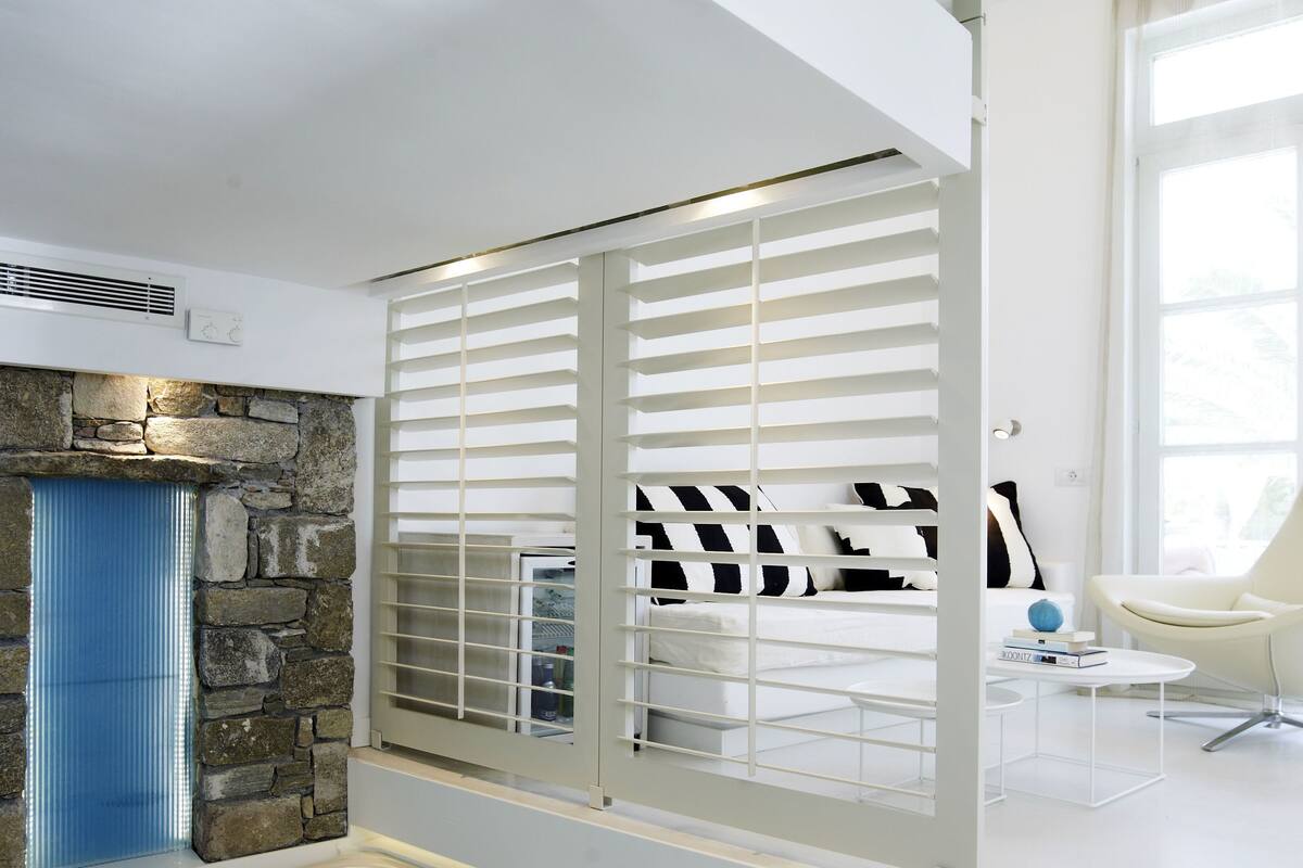 Un baño moderno con pared de piedra, una bañera y una ventana con persianas.