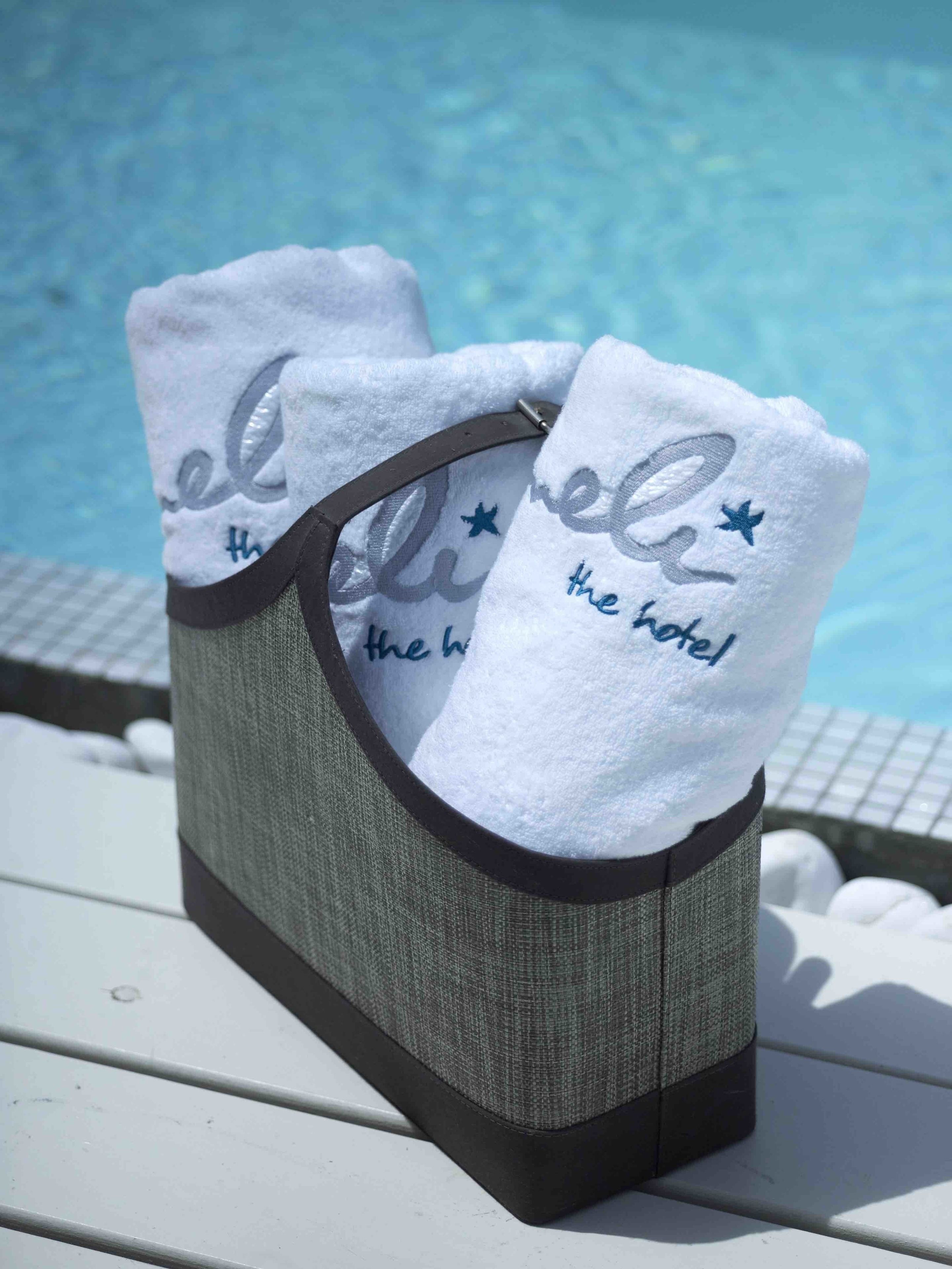 A poolside setting with a towel rack holding two white towels with embroidered text.