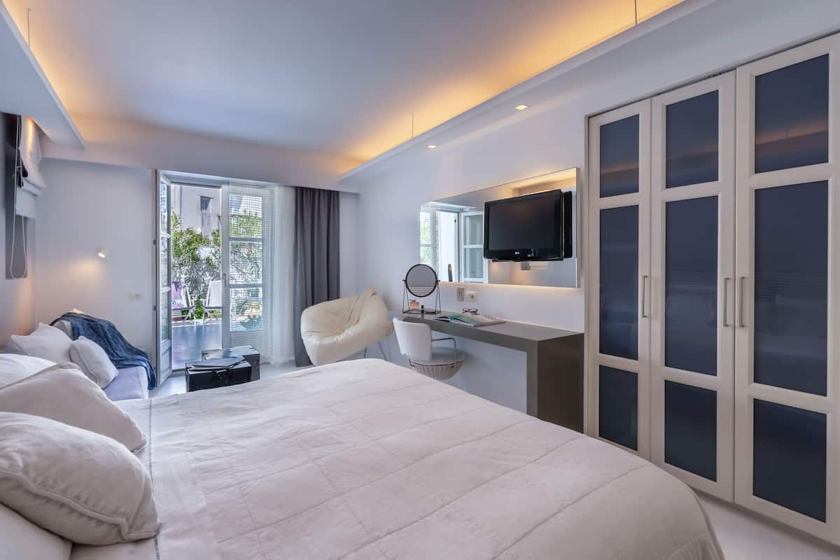 Una habitación de hotel moderna con una cama grande, un escritorio con televisor de pantalla plana, una silla y un armario.