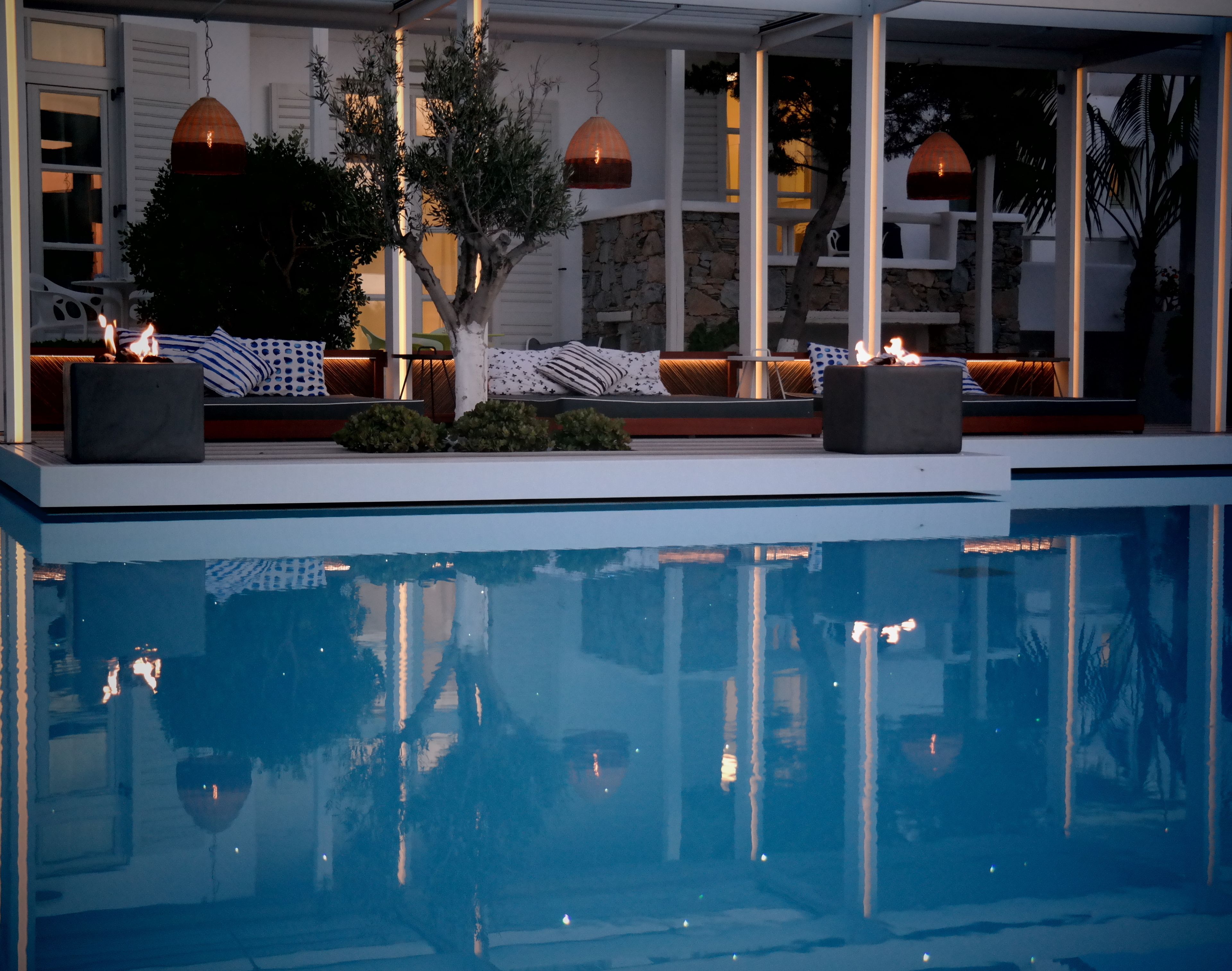A poolside area with a stone wall, seating, and hanging lamps.