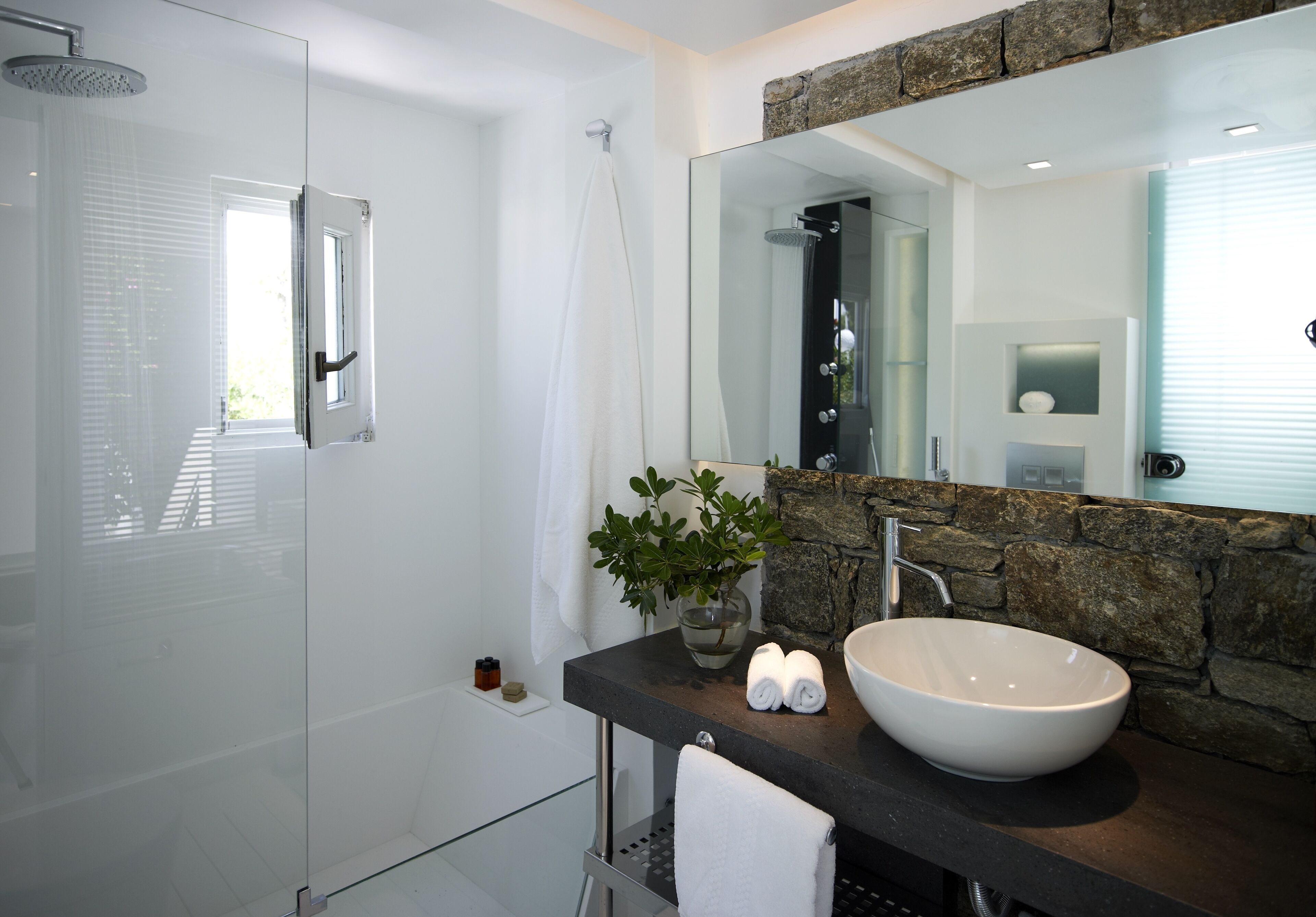 A modern bathroom with a glass shower enclosure, a large mirror, a stone accent wall, and a vessel sink.