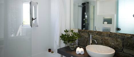 Een moderne badkamer met een glazen douchecabine, een grote spiegel, een accentmuur van steen en een wastafel.