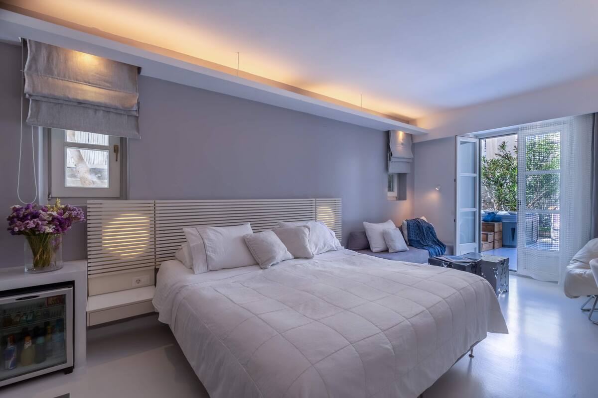 Un dormitorio moderno con una cama grande, mesitas de noche, una pequeña zona de estar y un balcón con vistas.