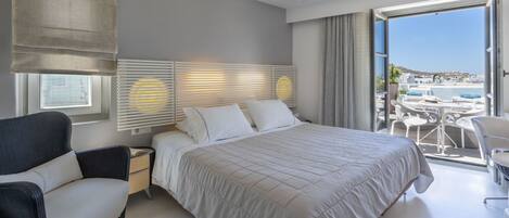 Un dormitorio moderno con una cama grande, una mesita de noche, una silla y un balcón con mobiliario exterior.