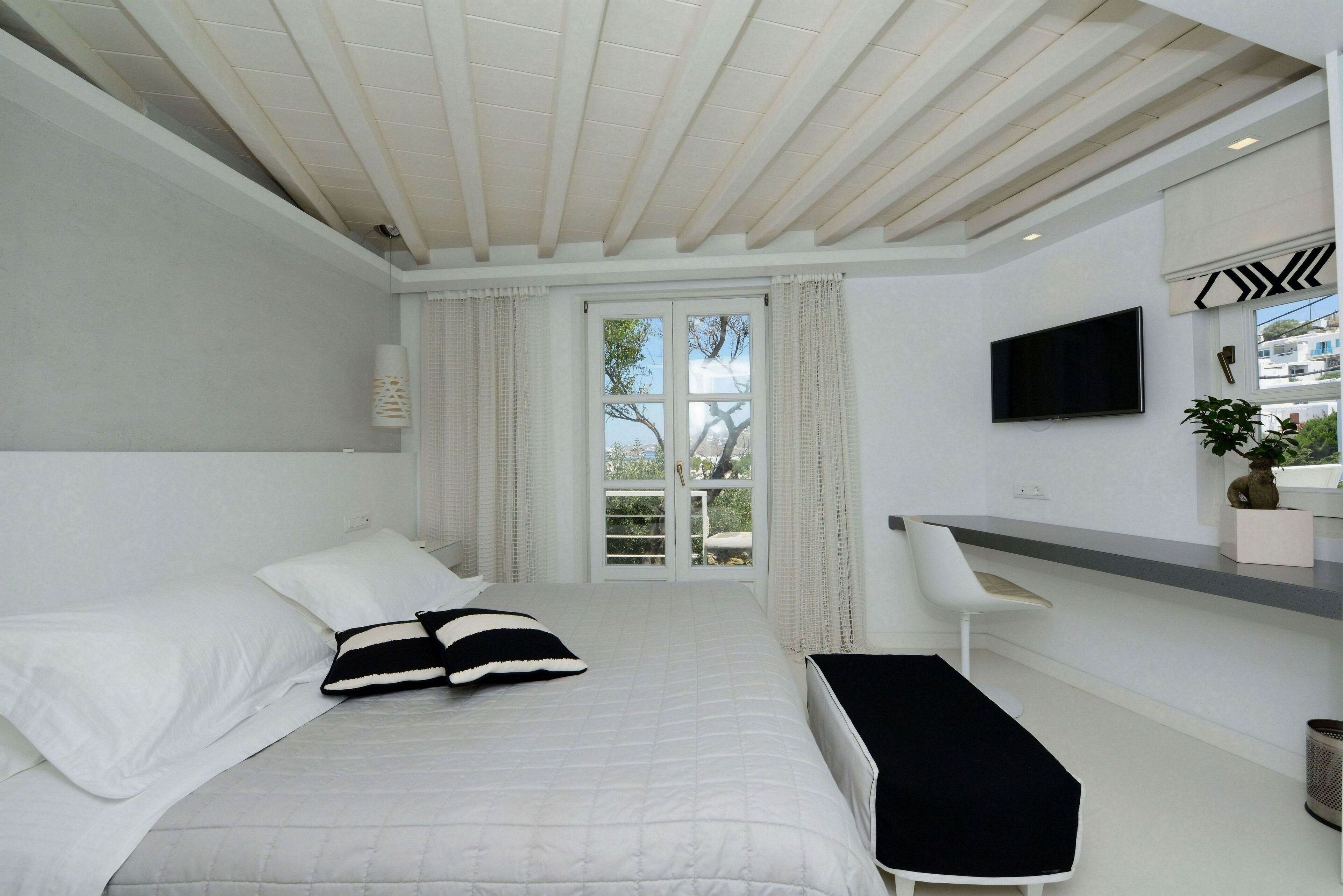 Une chambre moderne avec un lit, un banc, une télévision et une fenêtre avec des rideaux.