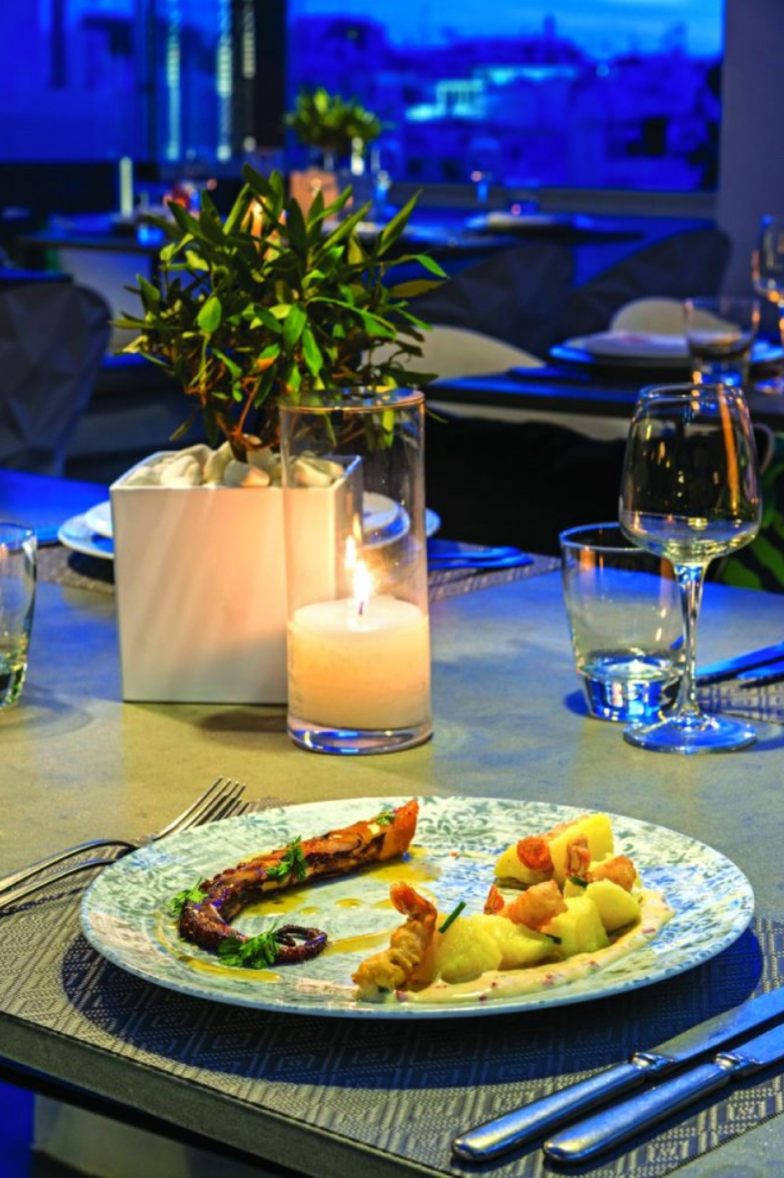Une table à manger avec une assiette de nourriture, une bougie et un verre d’eau.