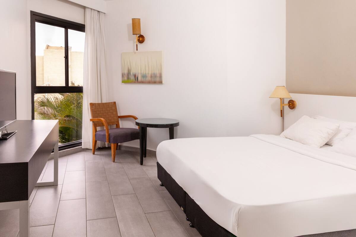 A hotel room with a bed, a desk, a chair, a small table, and a window with curtains.