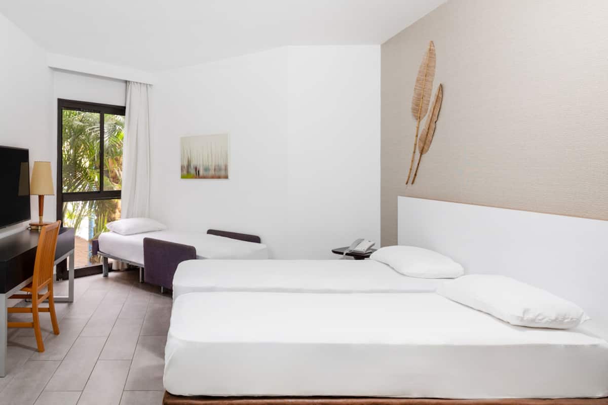 A hotel room with two beds, a desk with a chair, a TV, and a window with curtains.