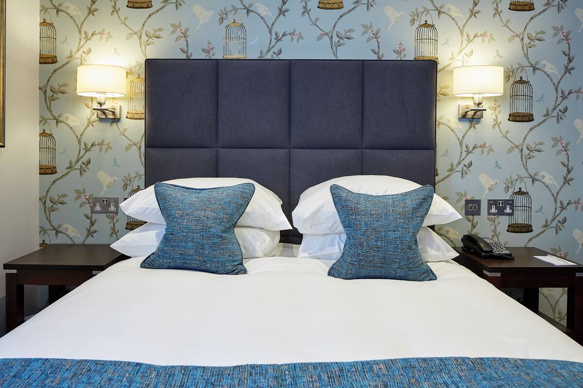 A hotel room with a large bed, two nightstands, a telephone, and wall sconces.