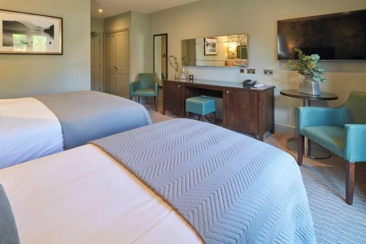 A hotel room with two beds, a desk, a chair, a TV, and a mirror.