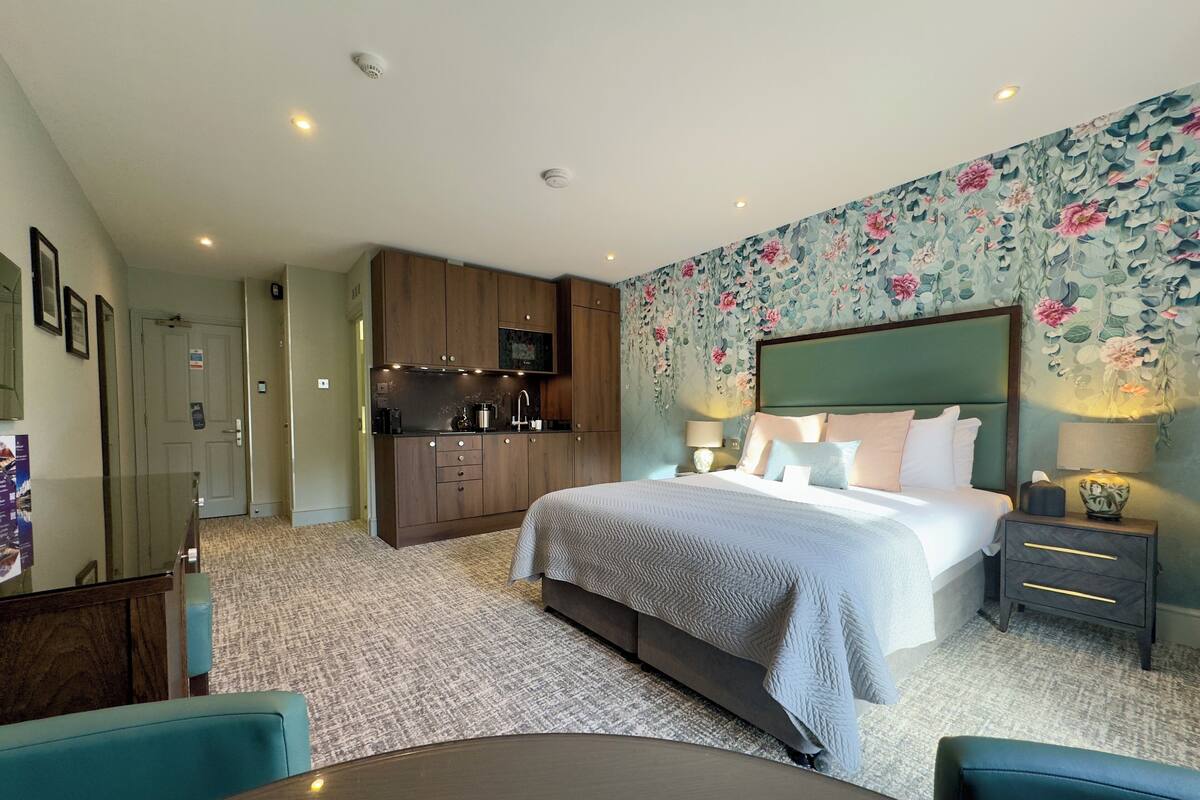 A hotel room with a bed, bedside tables, a desk, and a kitchenette.