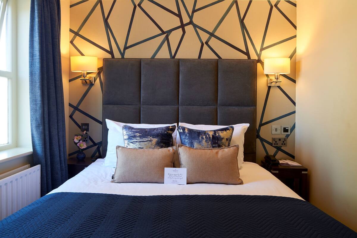 A hotel room with a large bed, two wall-mounted lamps, and a geometric-patterned wall.