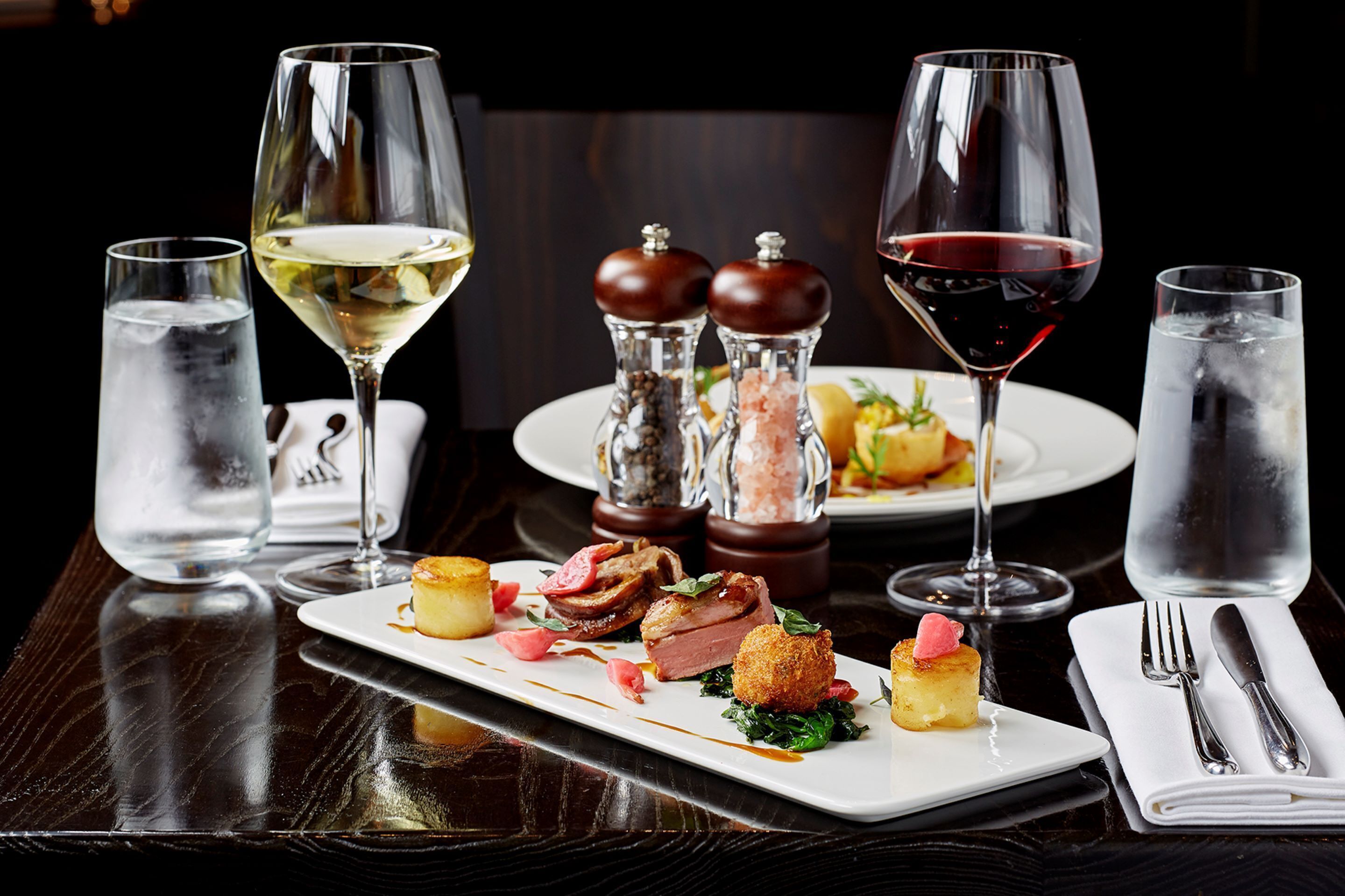 Une table à manger dressée avec une variété de plats, des verres de vin, ainsi que des salières et des poivrières.