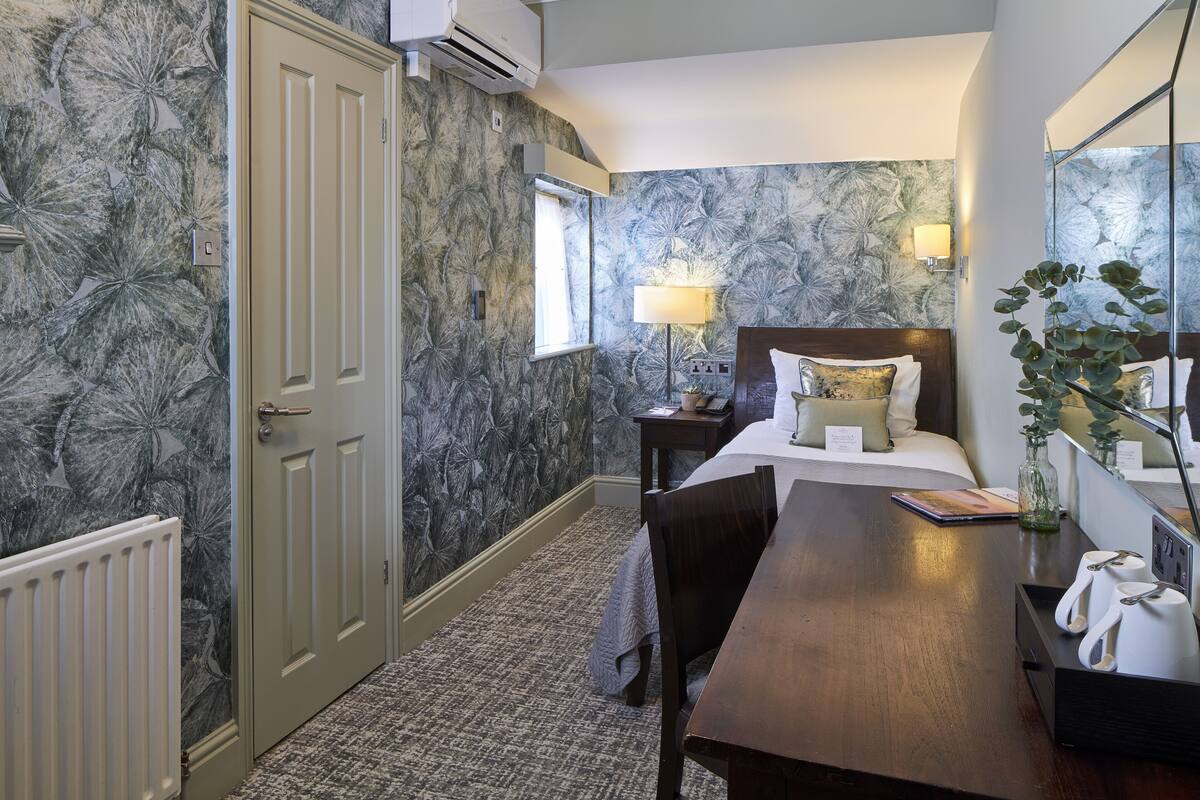 A hotel room with a bed, bedside table, lamp, and a mirror.