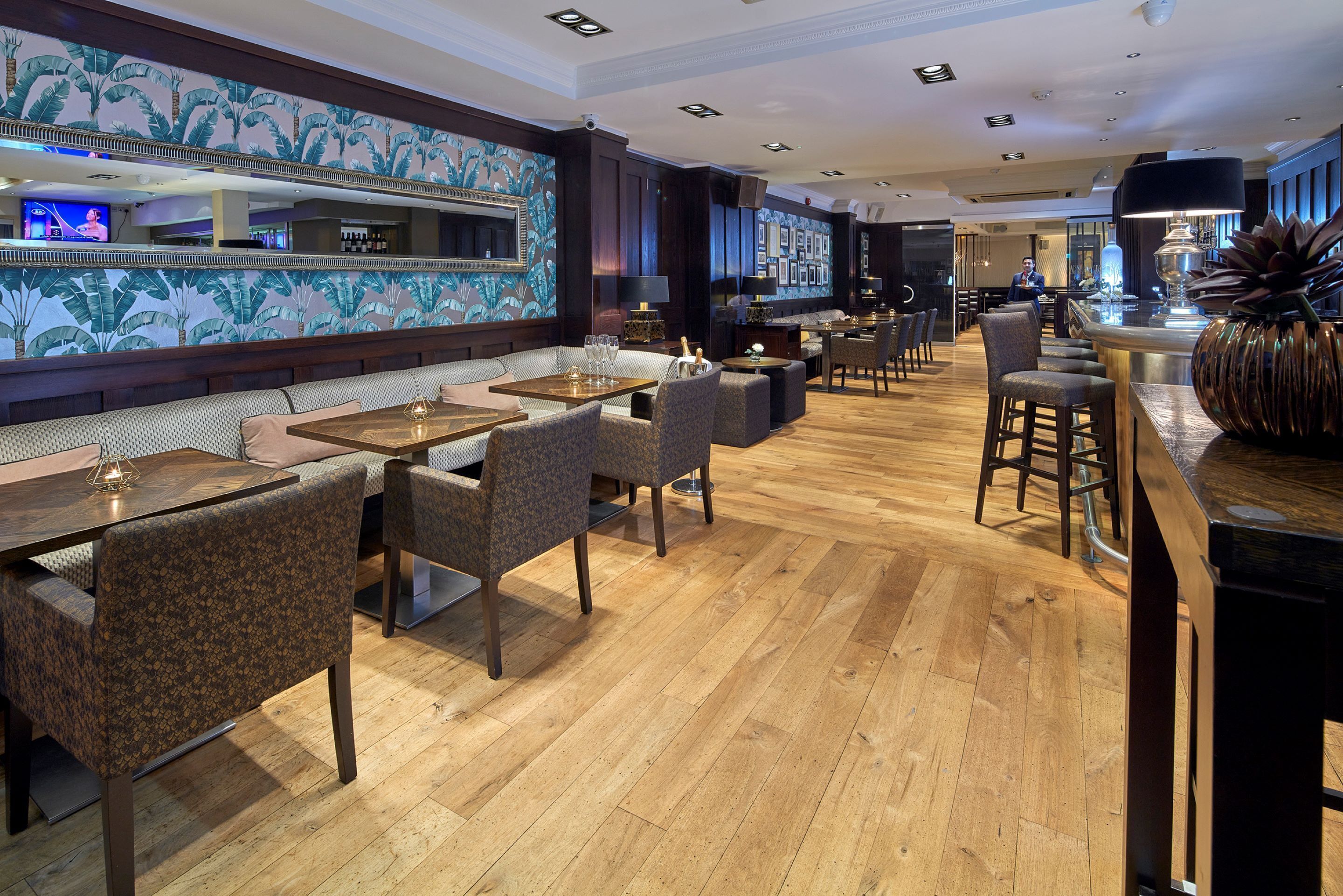 Un espace bar moderne avec un plancher en bois, des coins salon et un grand miroir qui reflète le bar.
