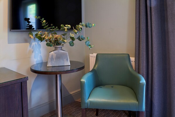 Una habitación con un sillón verde, una pequeña mesa redonda con un florero de plantas y un televisor de pantalla plana montado en la pared.