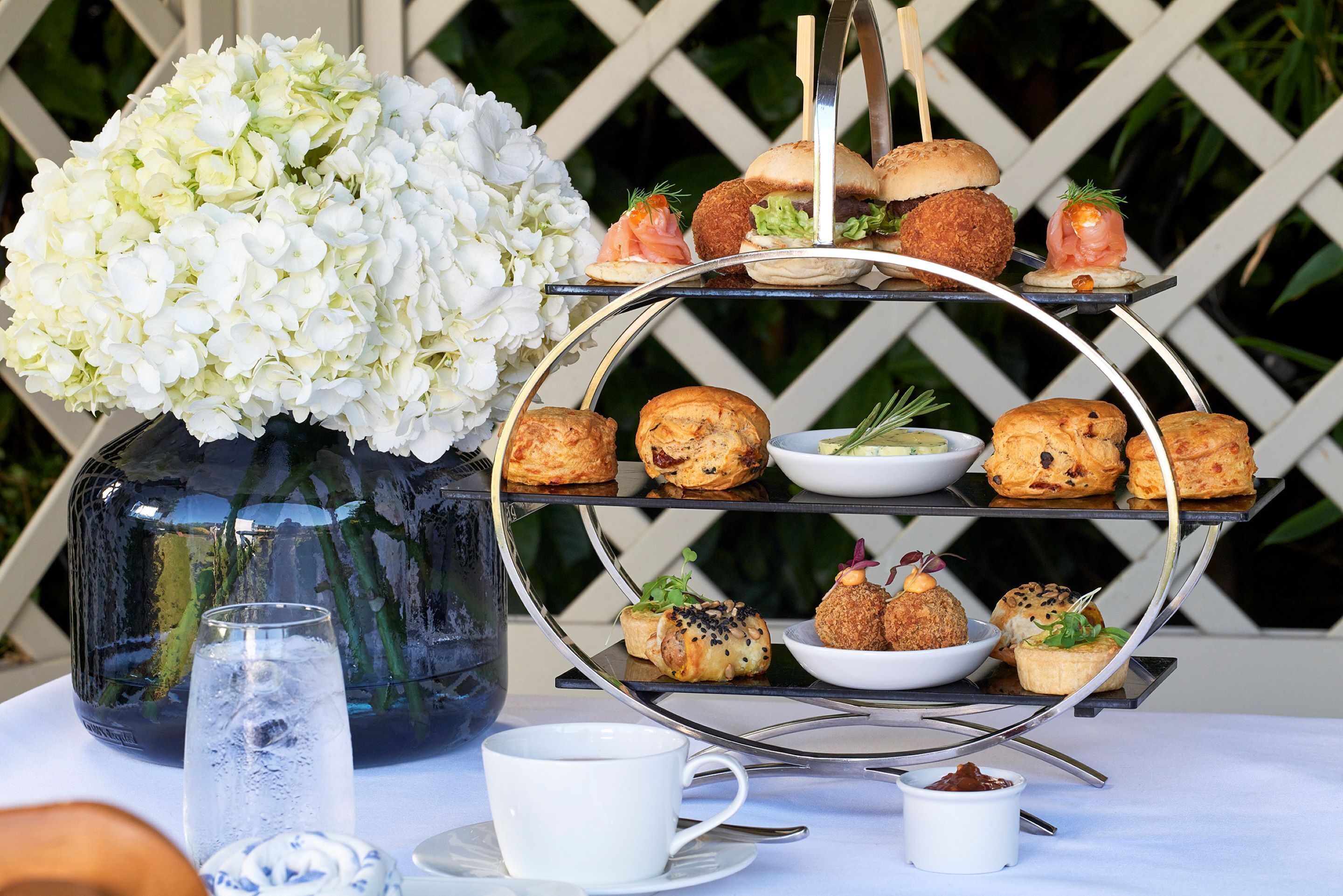 A three-tiered dessert stand with various pastries and a vase of white flowers.