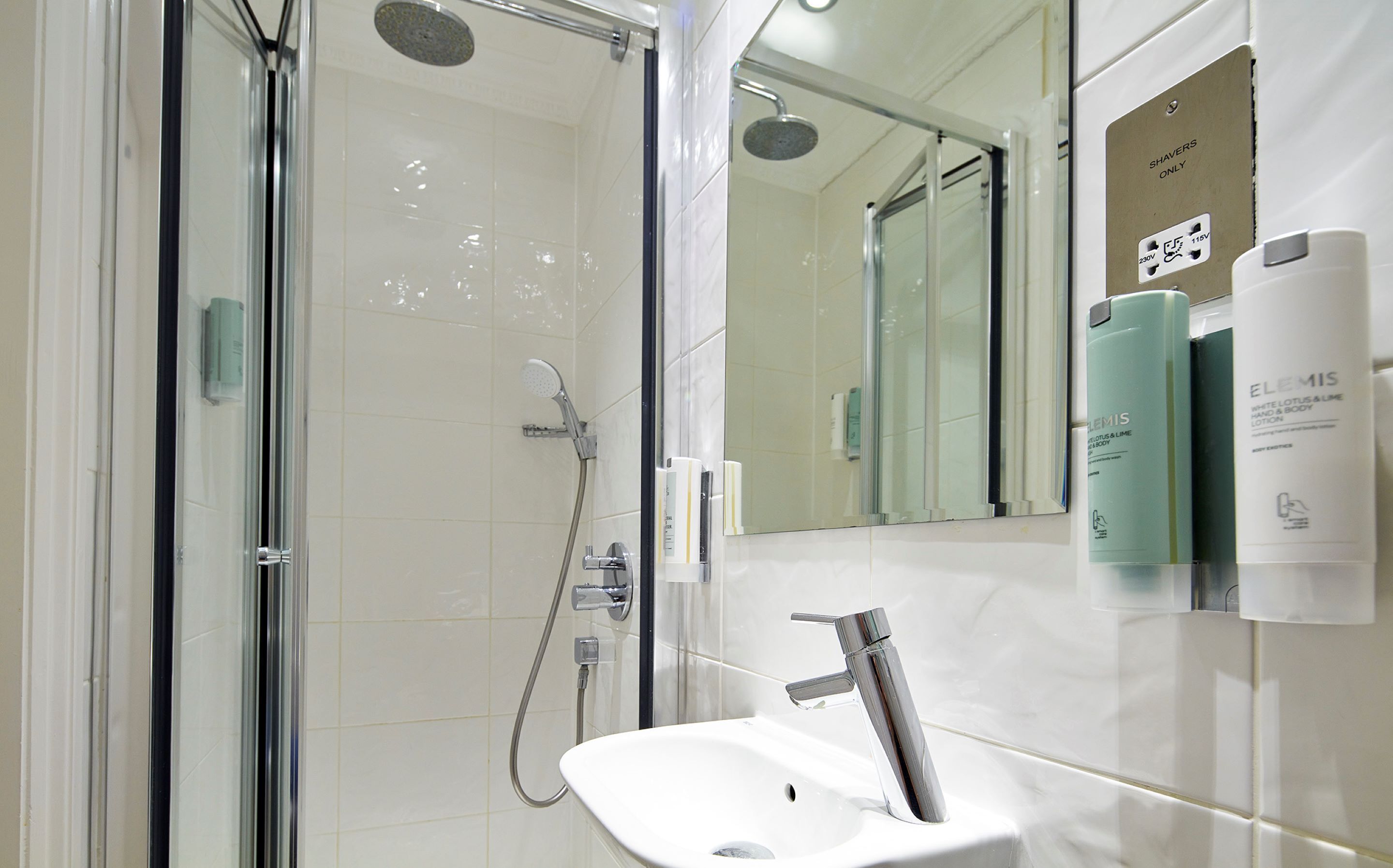 Un baño moderno con cabina de ducha de vidrio, un lavamanos blanco con grifo cromado y artículos de tocador en la pared.