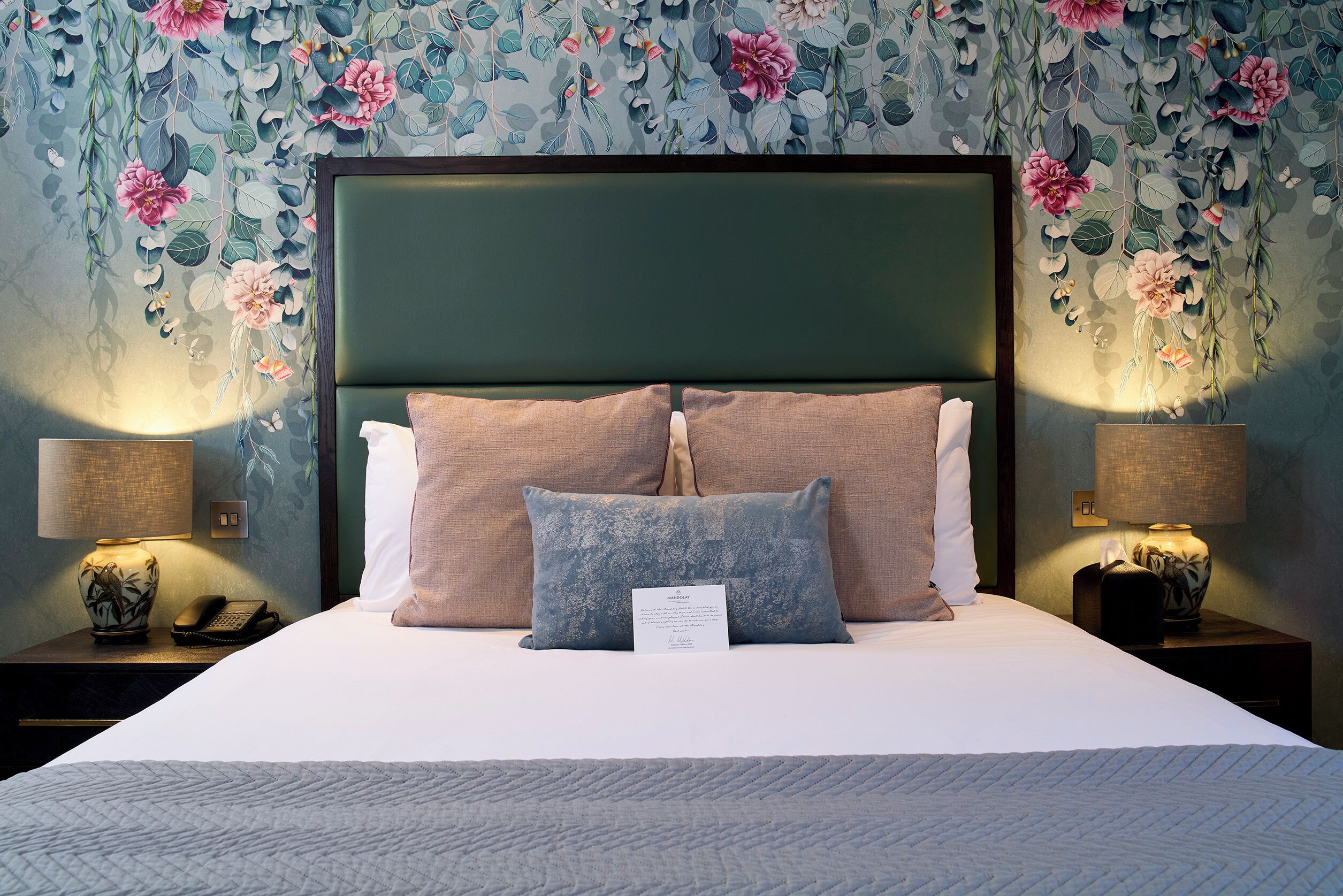 Een net opgemaakt bed met een groen hoofdeinde, twee kussens en een bedlampje aan weerszijden.
