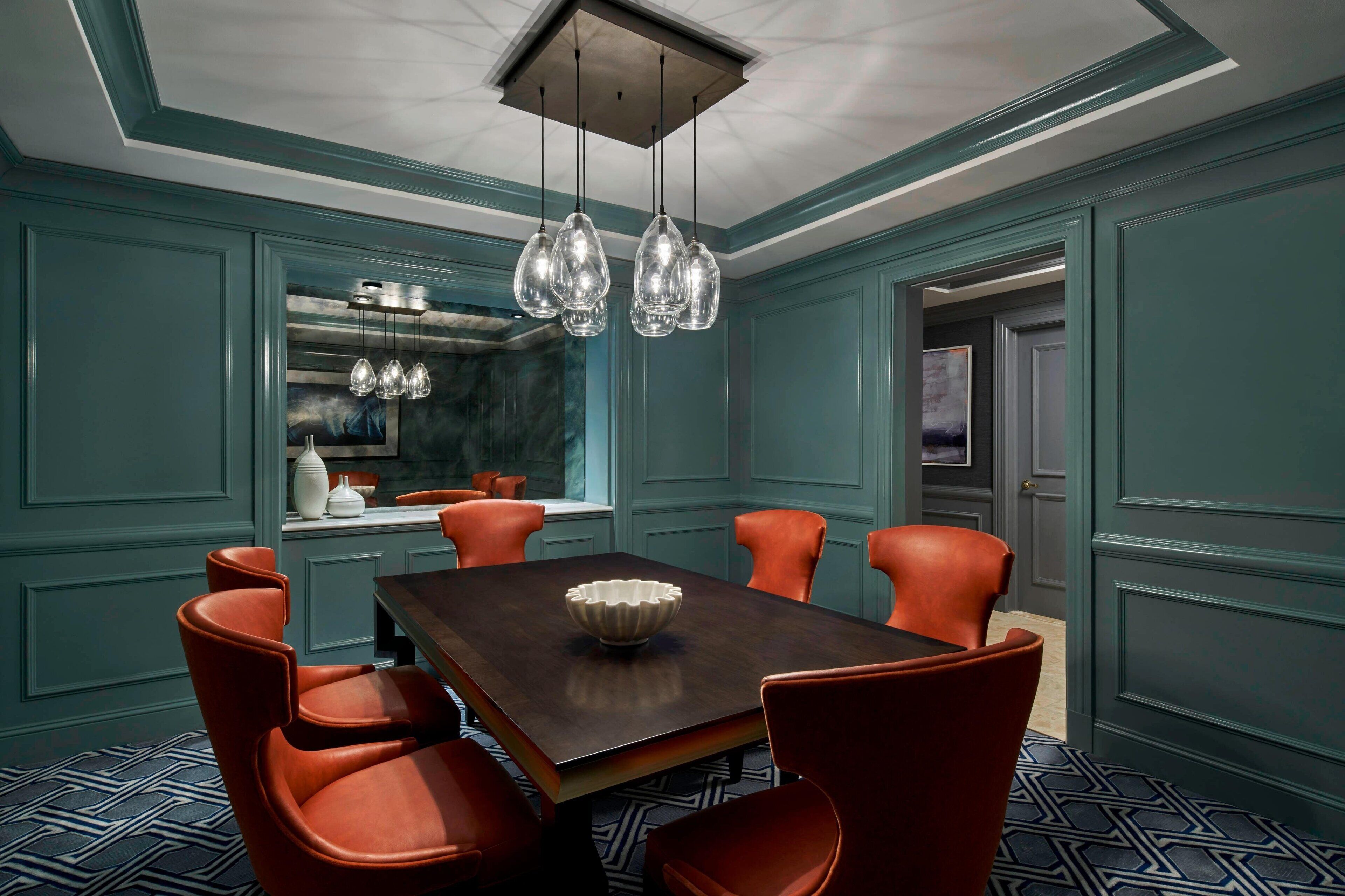 A dining area with a dark wooden table, six red chairs, and a hanging light fixture.