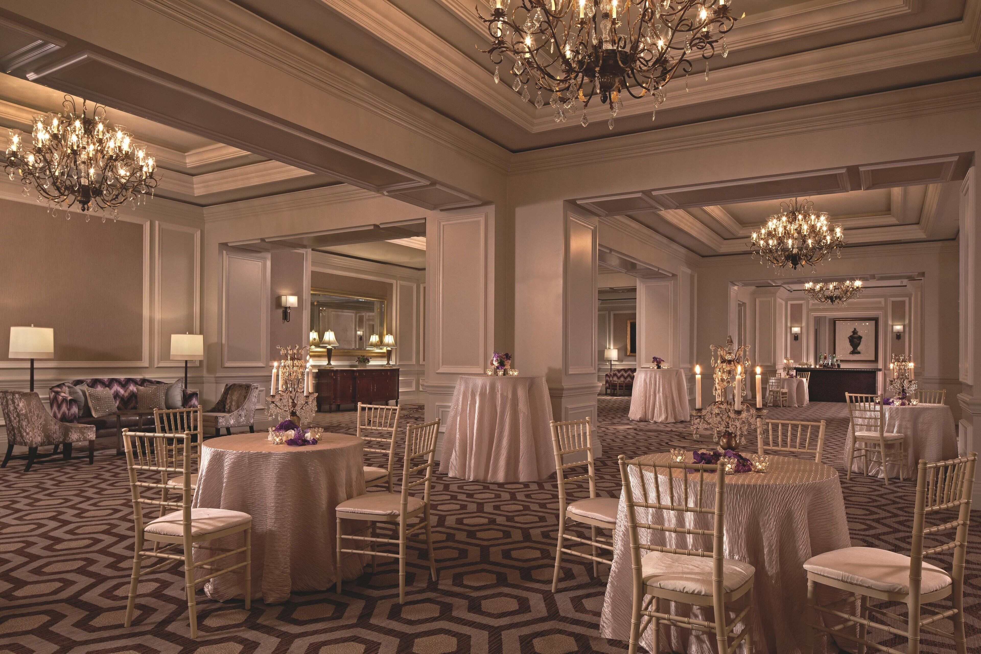 Ein prächtiger Ballsaal mit mehreren runden Tischen, eleganten Kronleuchtern und einem gemusterten Teppich.