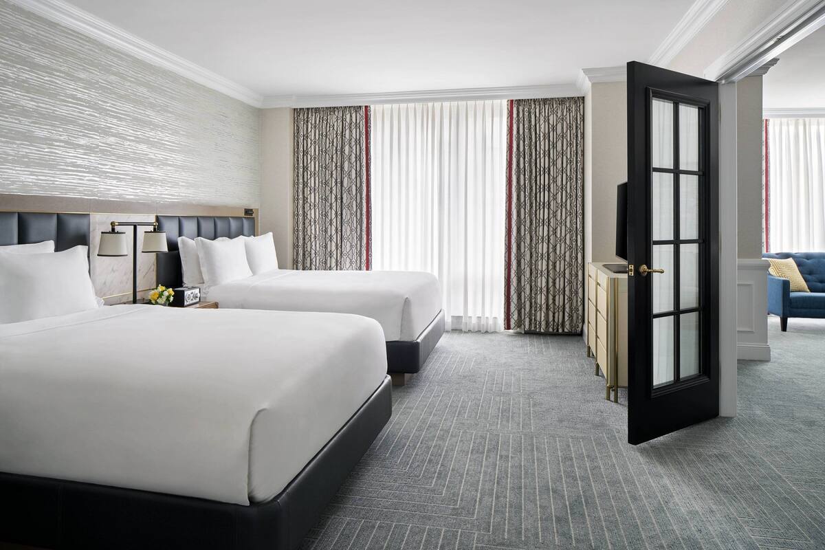A hotel room with two beds, a television, and a door leading to another room.