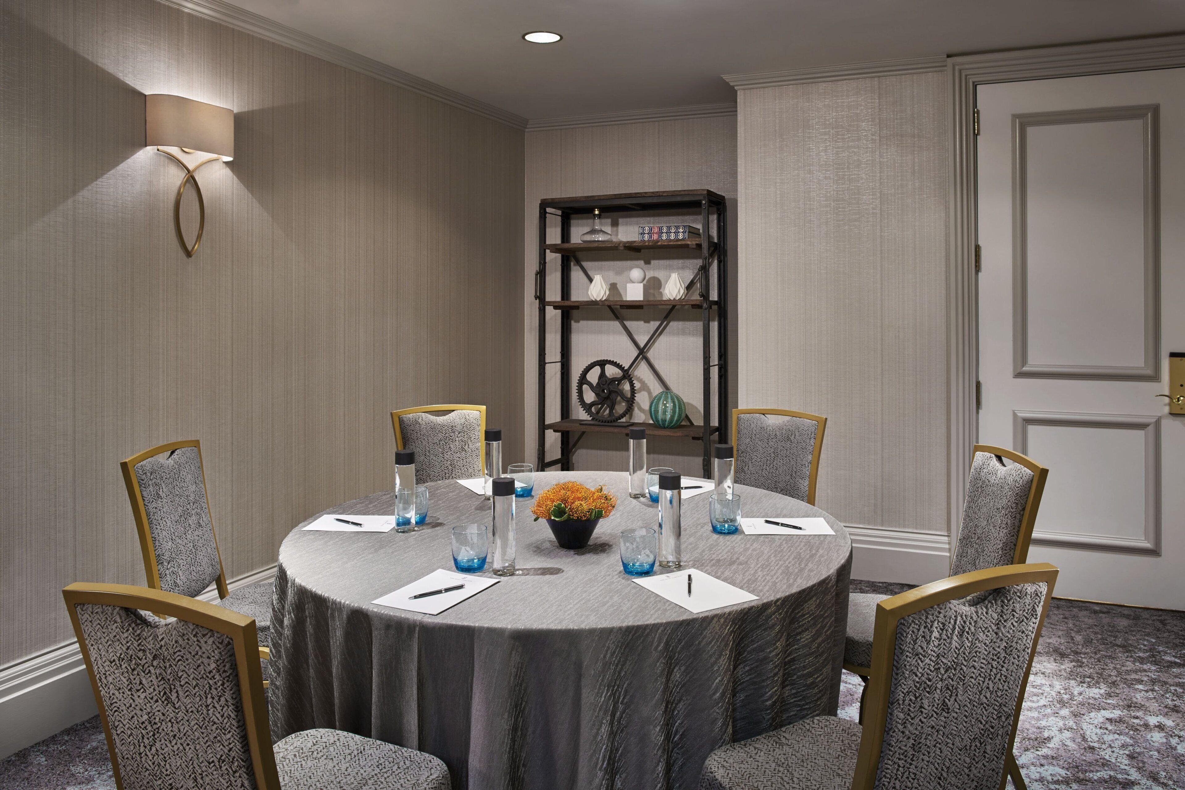 A conference room with a round table, six chairs, a bookshelf, and a vase with flowers.