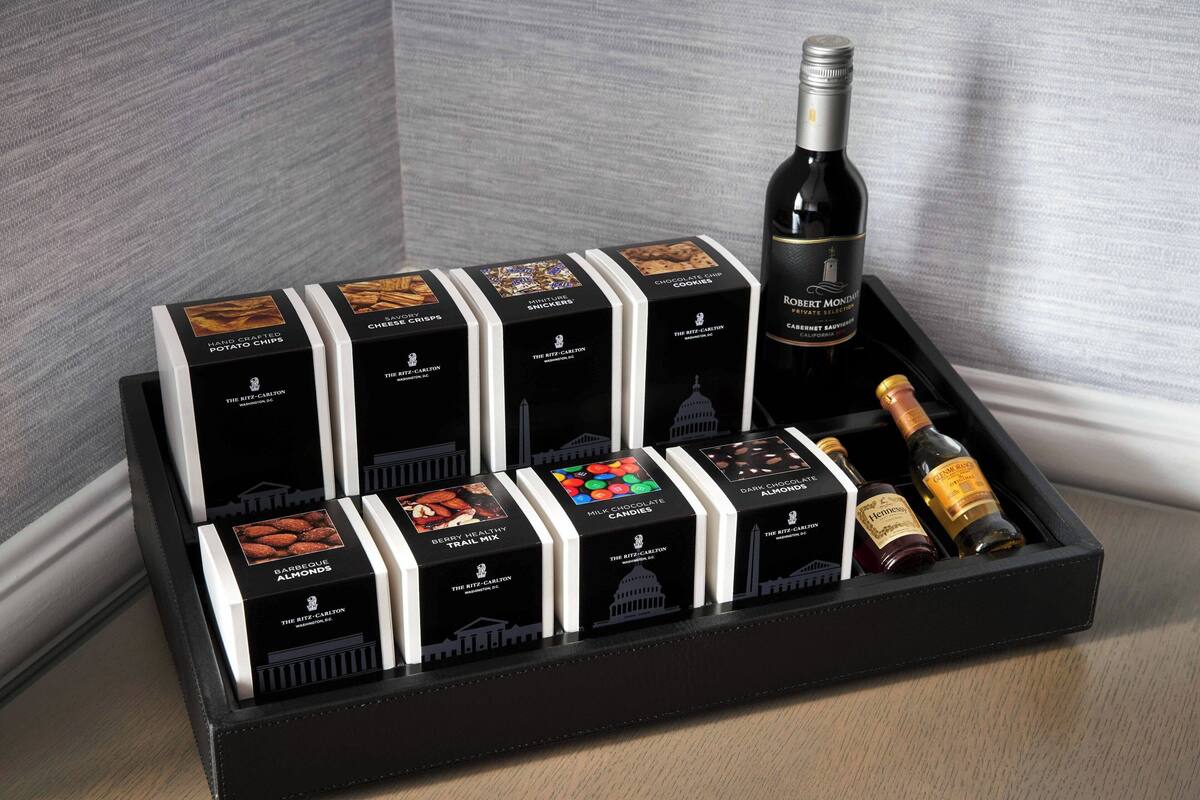A black gift box with various items including chocolate, a bottle of wine, and a bottle of liquor.