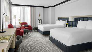 A hotel room with two beds, a desk, a chair, a small table, and a lamp.