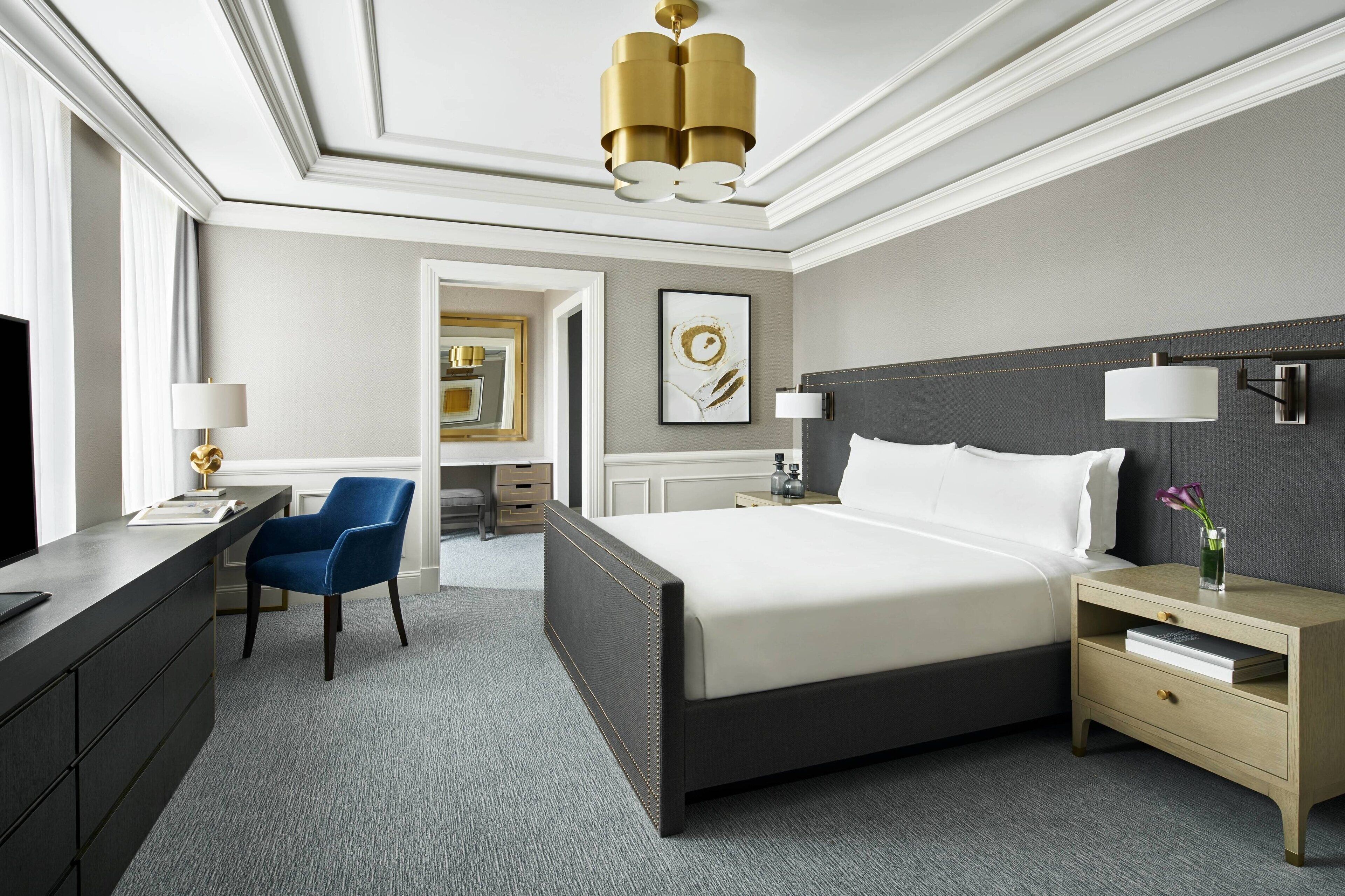 Quarto de hotel moderno com uma cama grande, mesas de cabeceira, uma escrivaninha e uma cadeira.