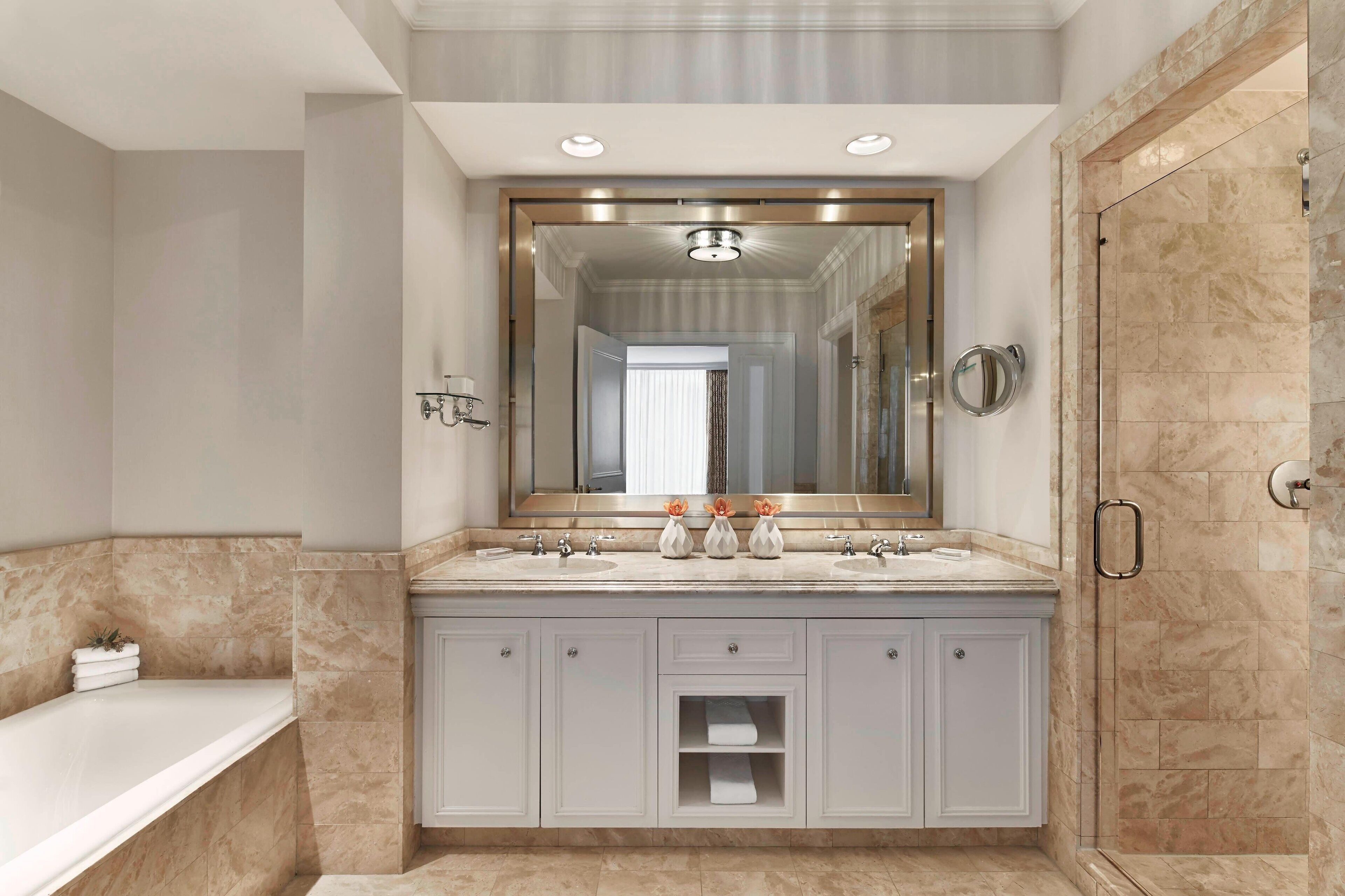 A modern bathroom with a large mirror, two sinks, a bathtub, and a walk-in shower.