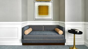 A corner seating area with a patterned sofa, a framed artwork on the wall, and a small round table with a book.