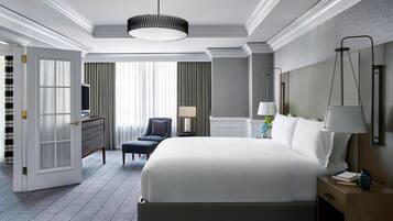 A hotel room with a large bed, a desk, a chair, and a nightstand with a lamp.
