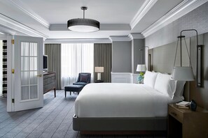 A hotel room with a large bed, a desk, a chair, and a nightstand with a lamp.