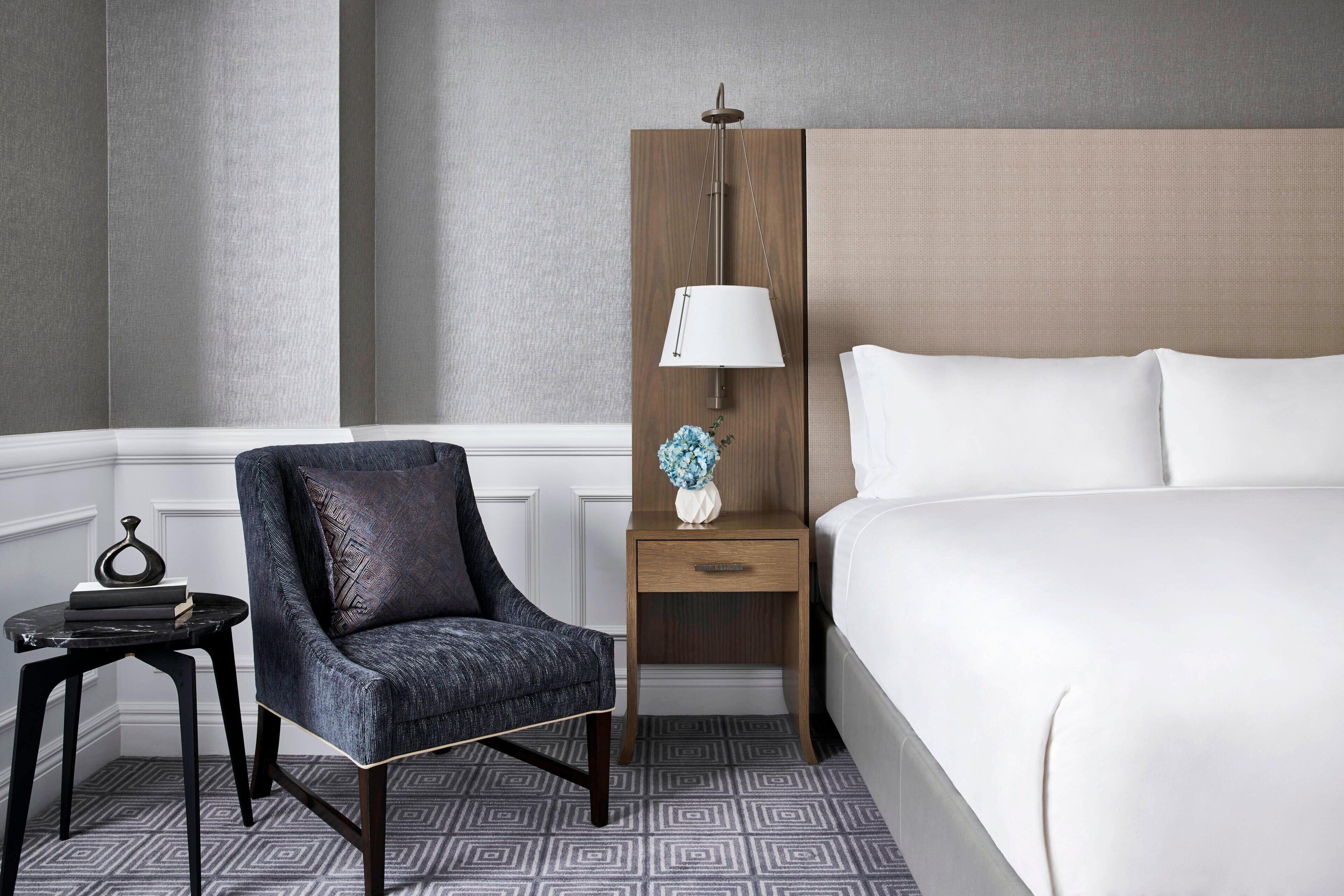 A hotel room with a bed, a chair, a nightstand, and a lamp.
